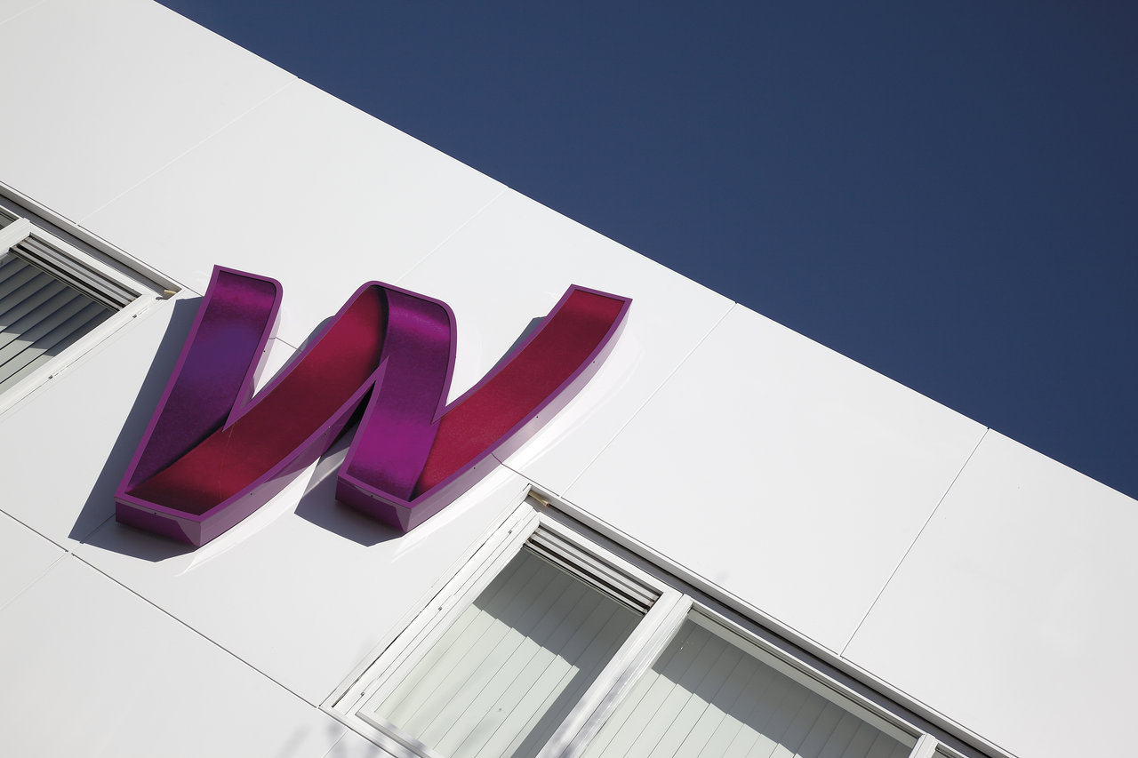 Stylized purple 'W' on modern white building facade, blue sky.