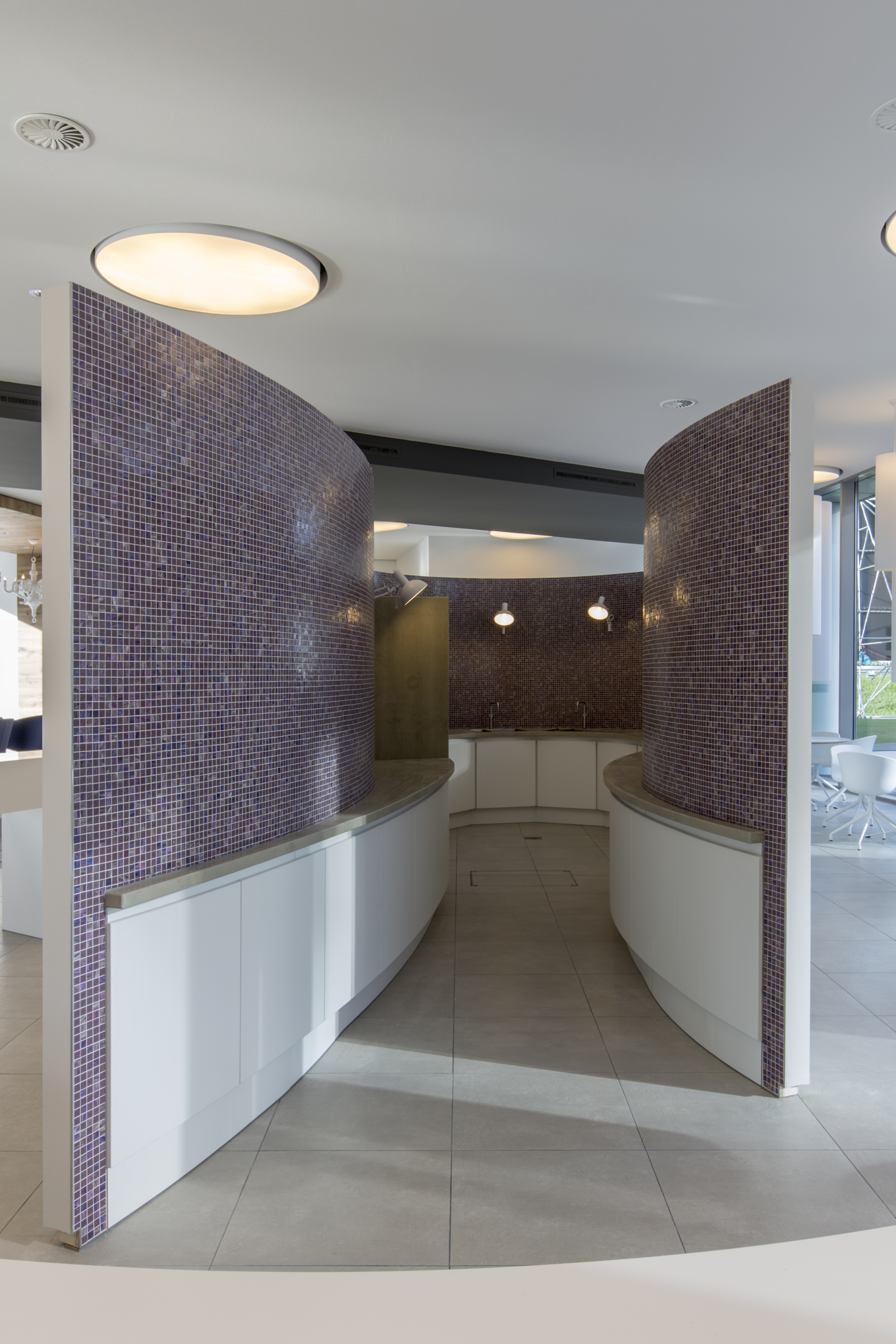 Curved room divider with purple mosaic tiles and light tiled floor.