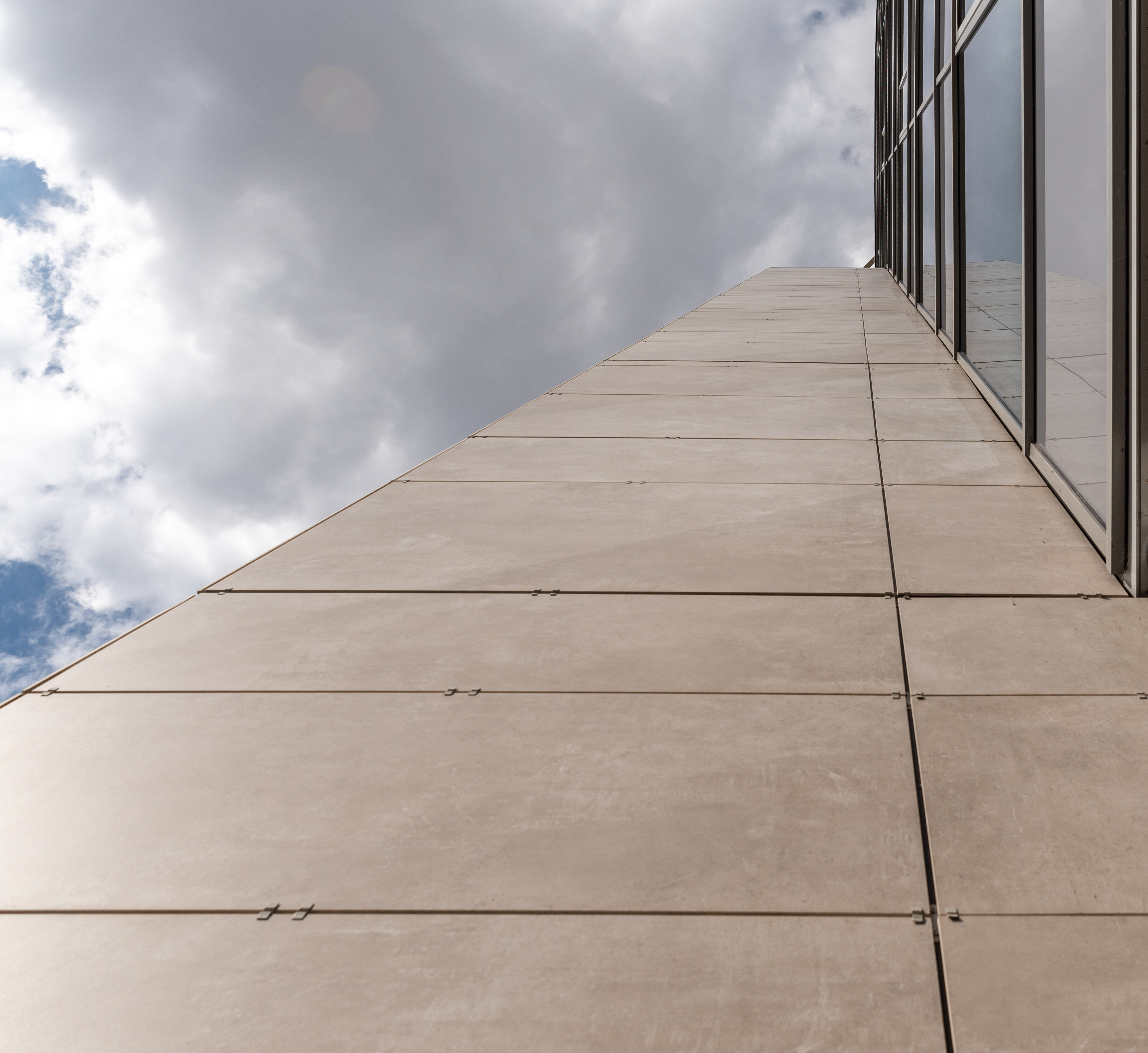 Modern building facade with bright, large-format tiles under a cloudy sky.