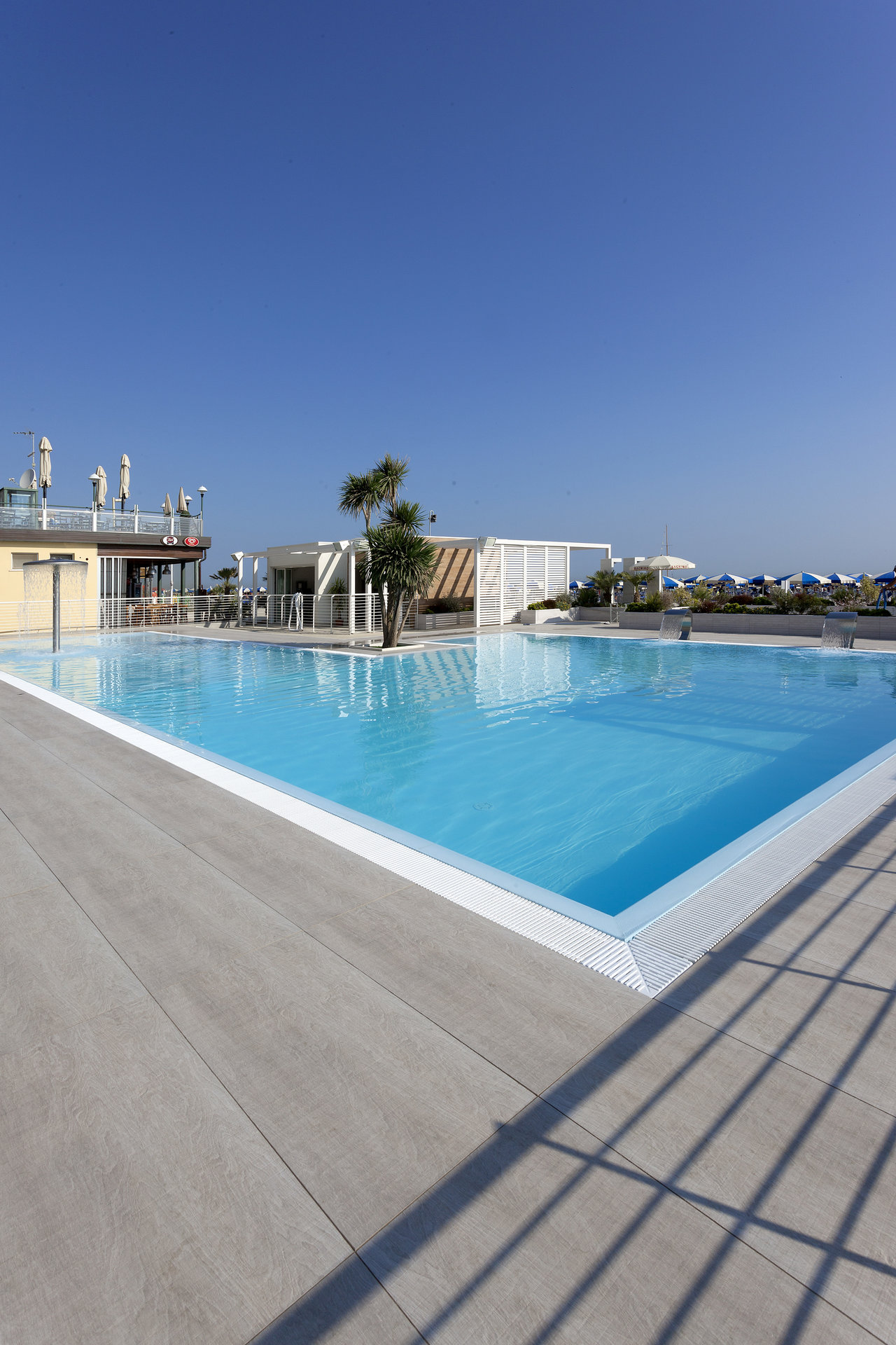 Graue Outdoor-Fliesen am Pool unter klarem Himmel.