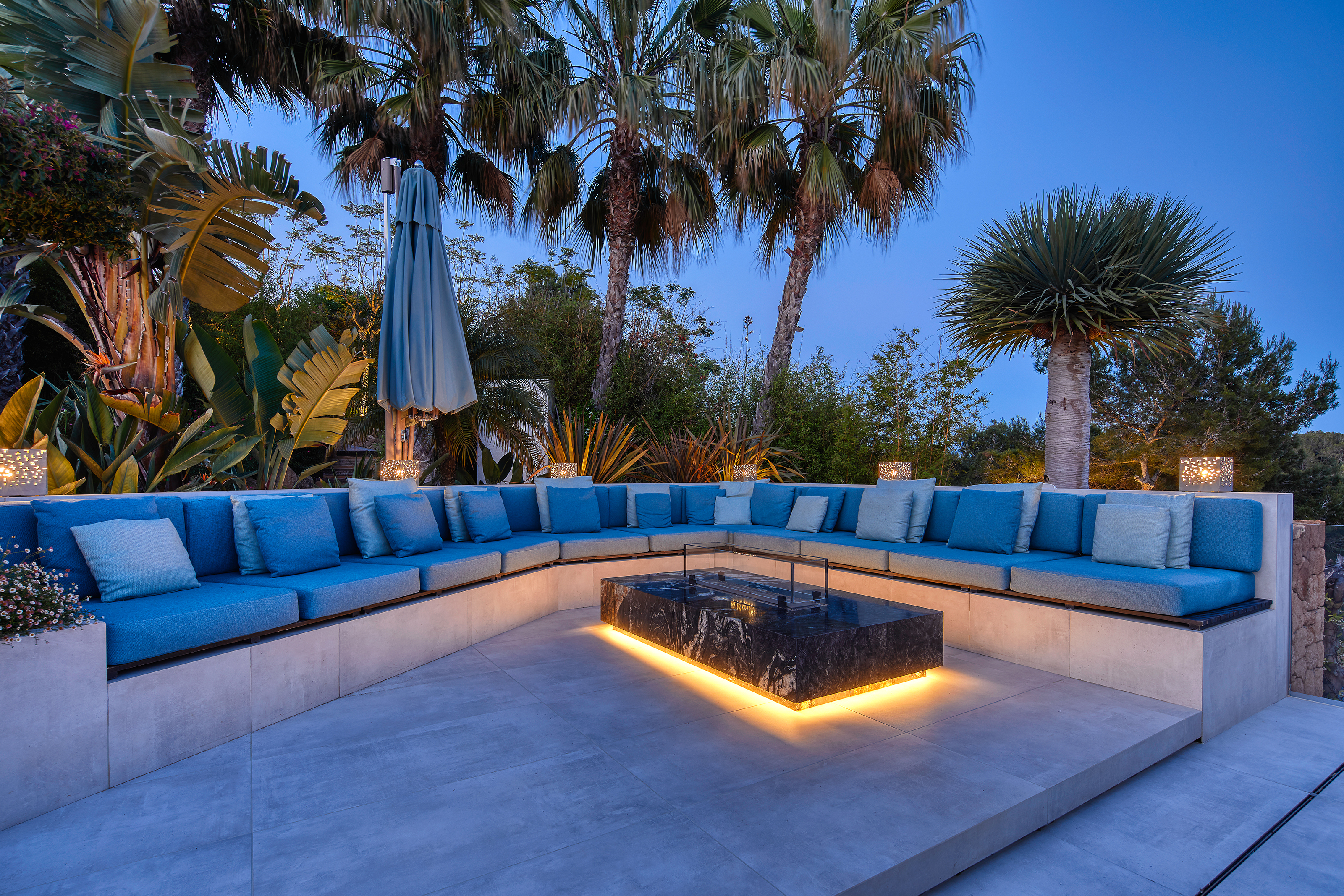 Luxurious terrace with modern outdoor tiles, blue lounge, and palm trees in evening light.