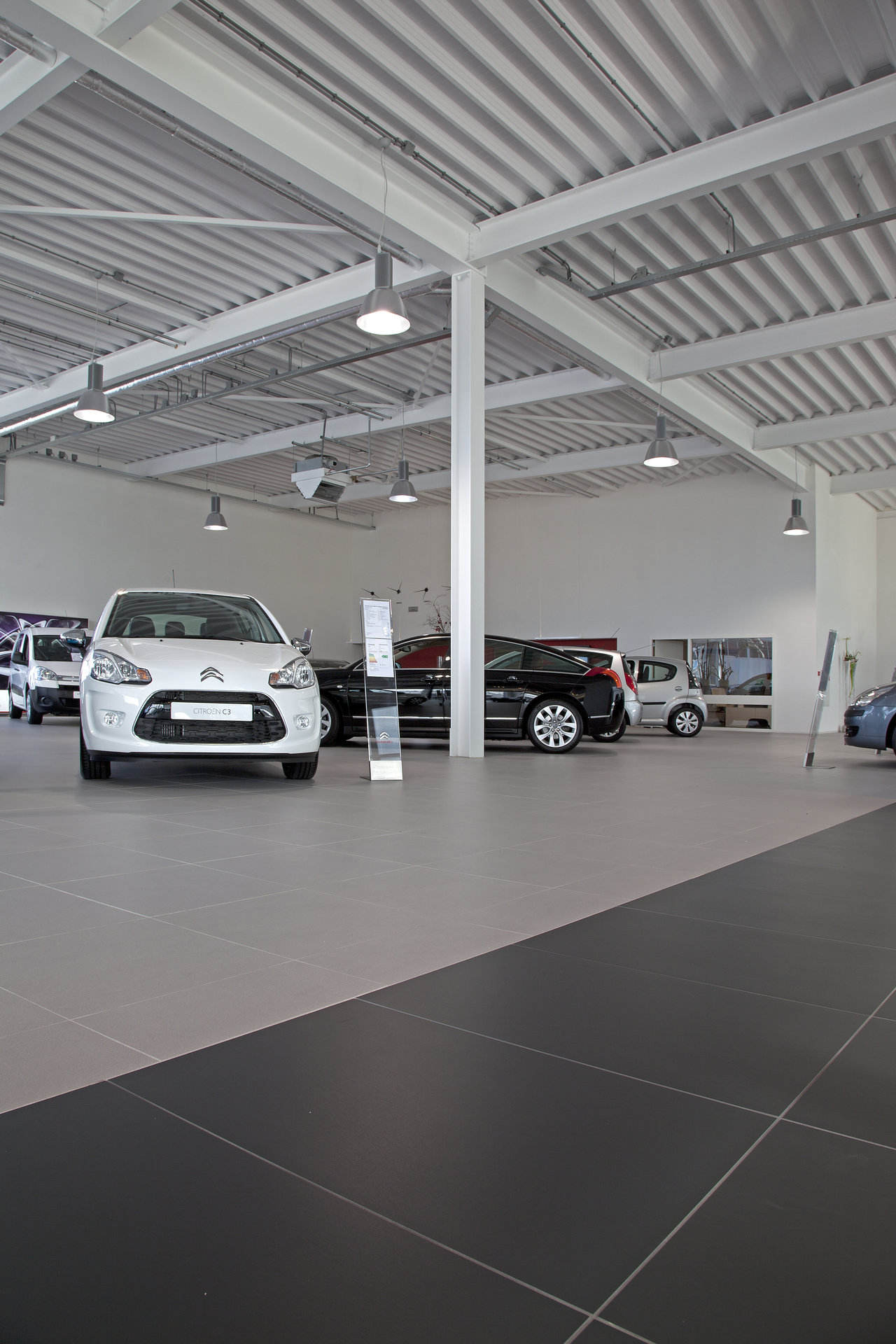 Large-format tiles in light grey and anthracite in a car dealership showroom.