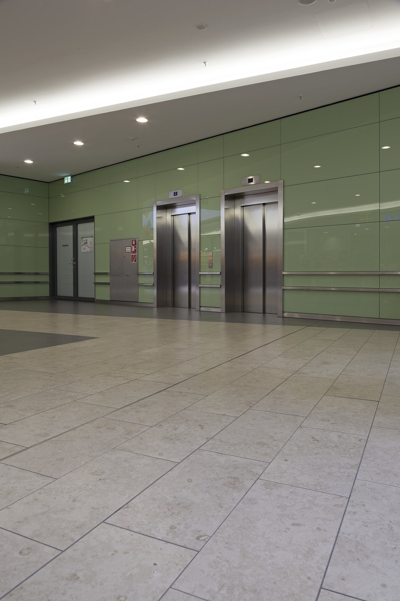 Large-format, light floor tiles in a modern building with lifts and a green wall.