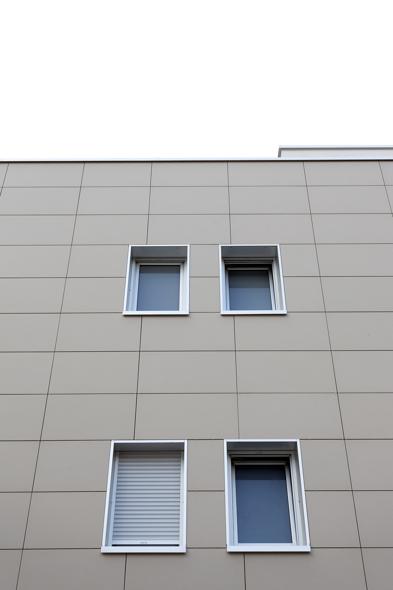 Modern building facade with large-format, beige tiles and four windows.