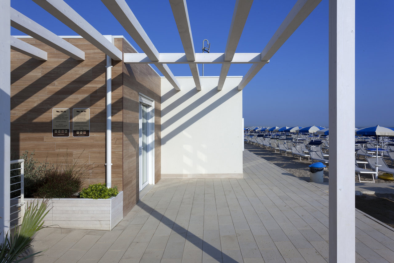Light outdoor tiles and wood-effect wall tiles on a sunny beach terrace with a pergola.