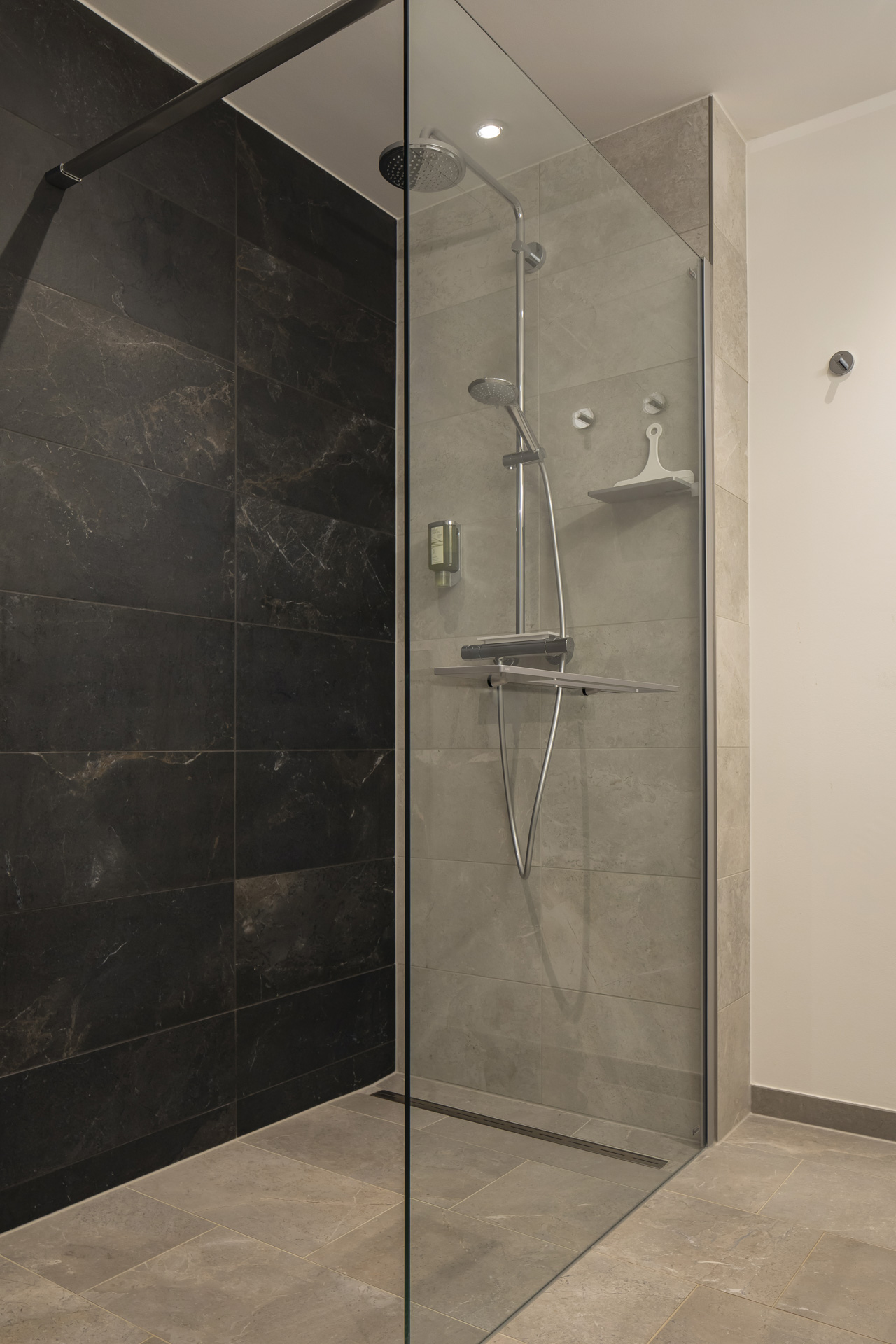 High-quality tiles in a modern shower cubicle: dark wall tiles and light grey floor and wall tiles.