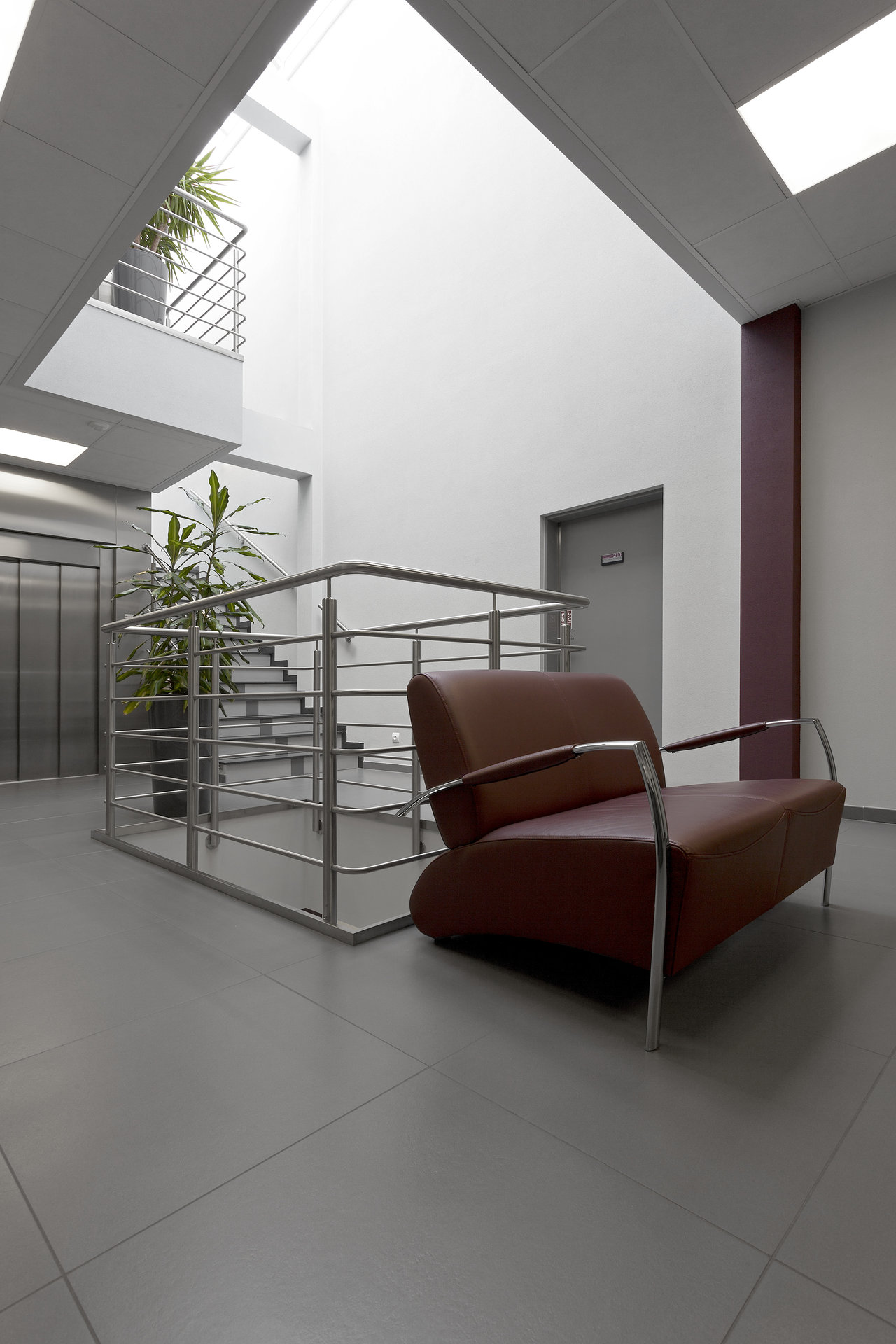 Large-format grey tiles in a modern foyer with a leather armchair and stairs.