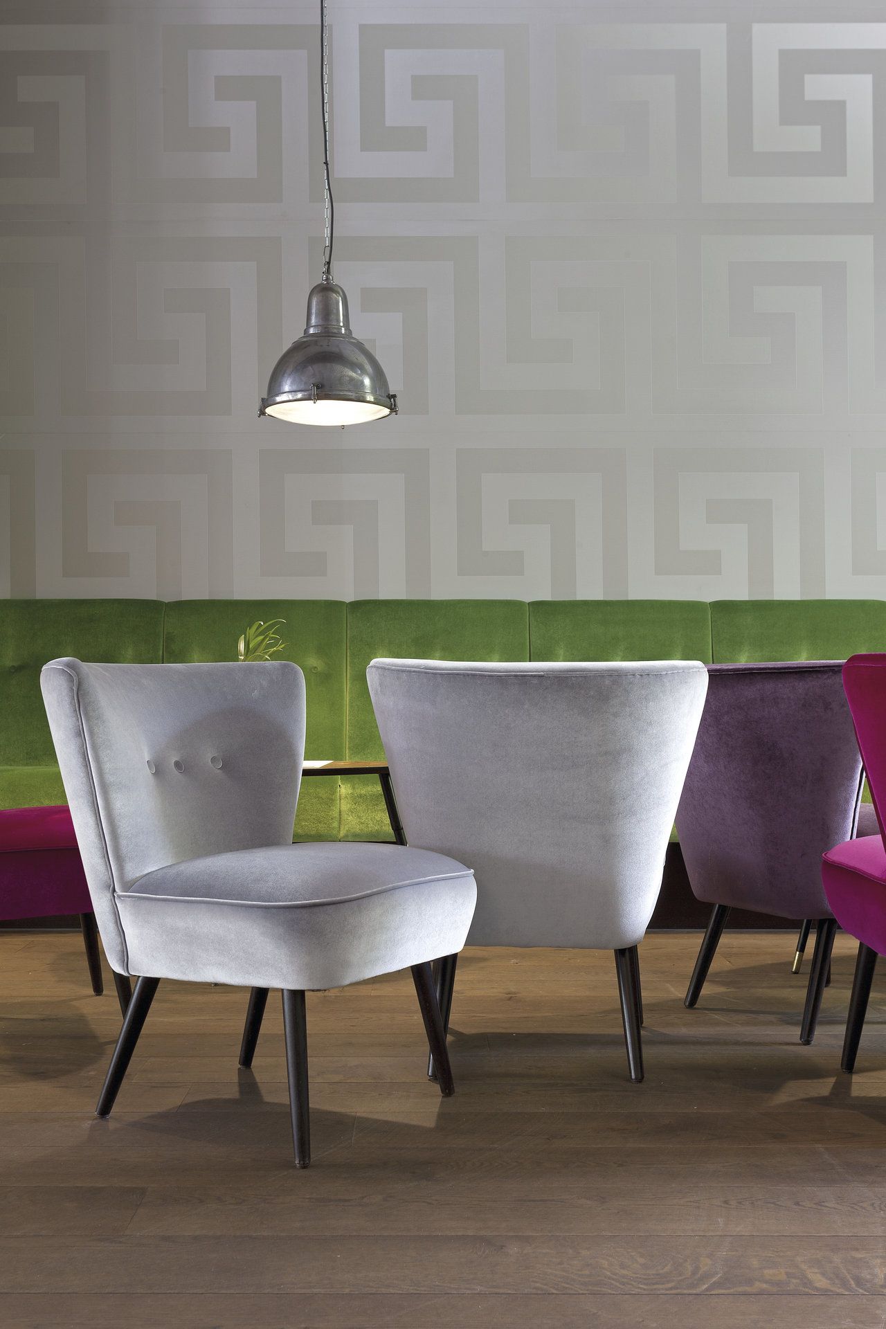 Dark wood-look tiles in a modern room with velvet chairs and a patterned wall.