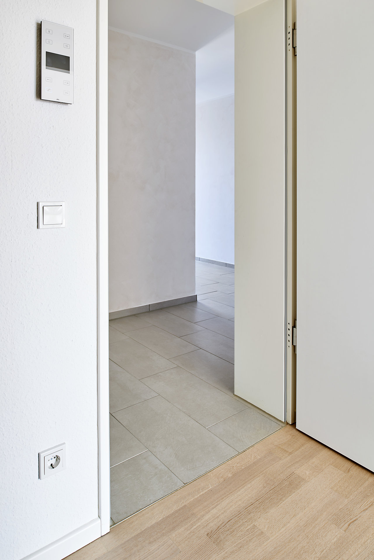 Light, rectangular hallway tiles, transitioning to wood flooring.
