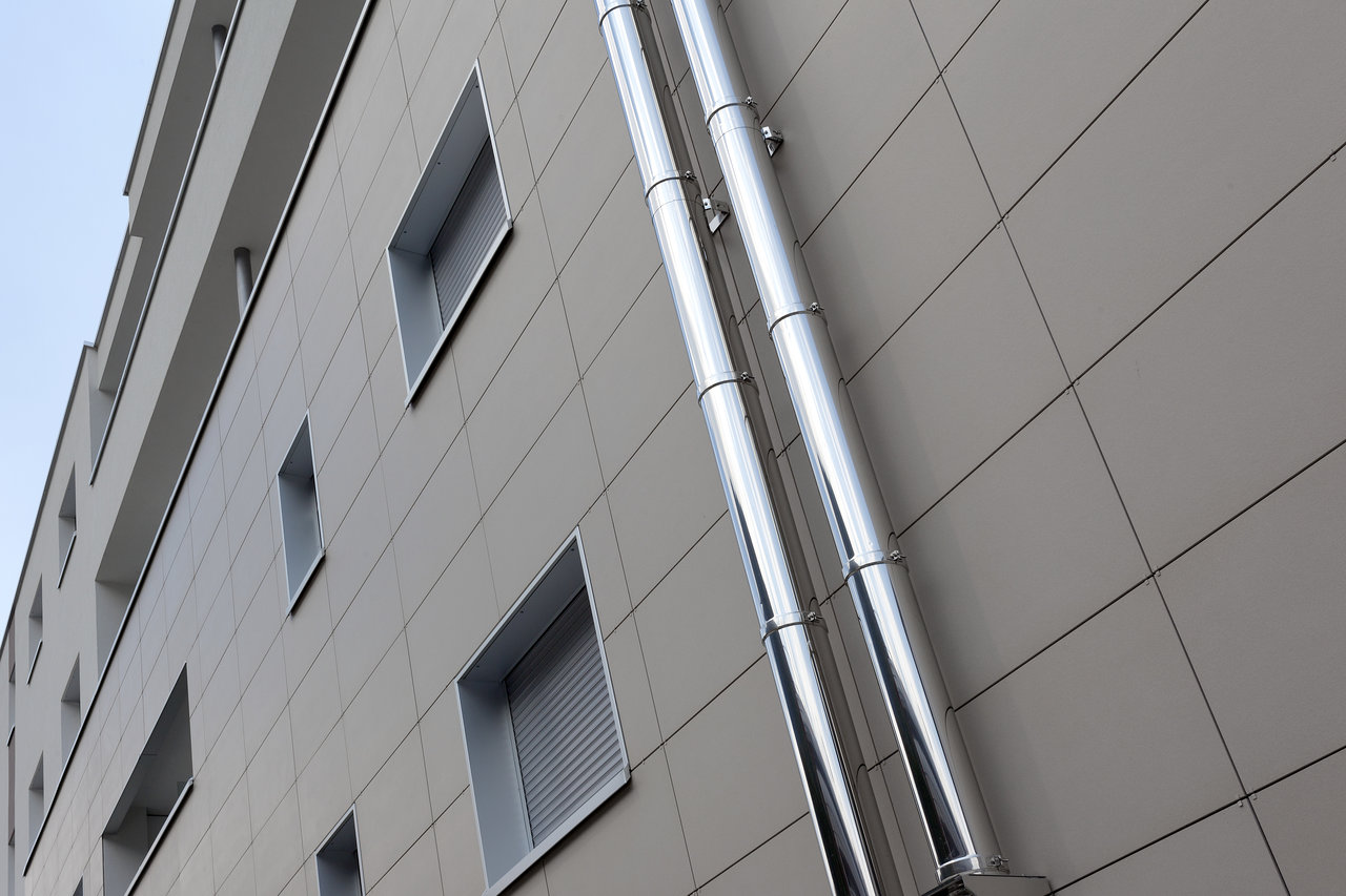 Modern exterior facade with light, rectangular tiles and vertical pipes.
