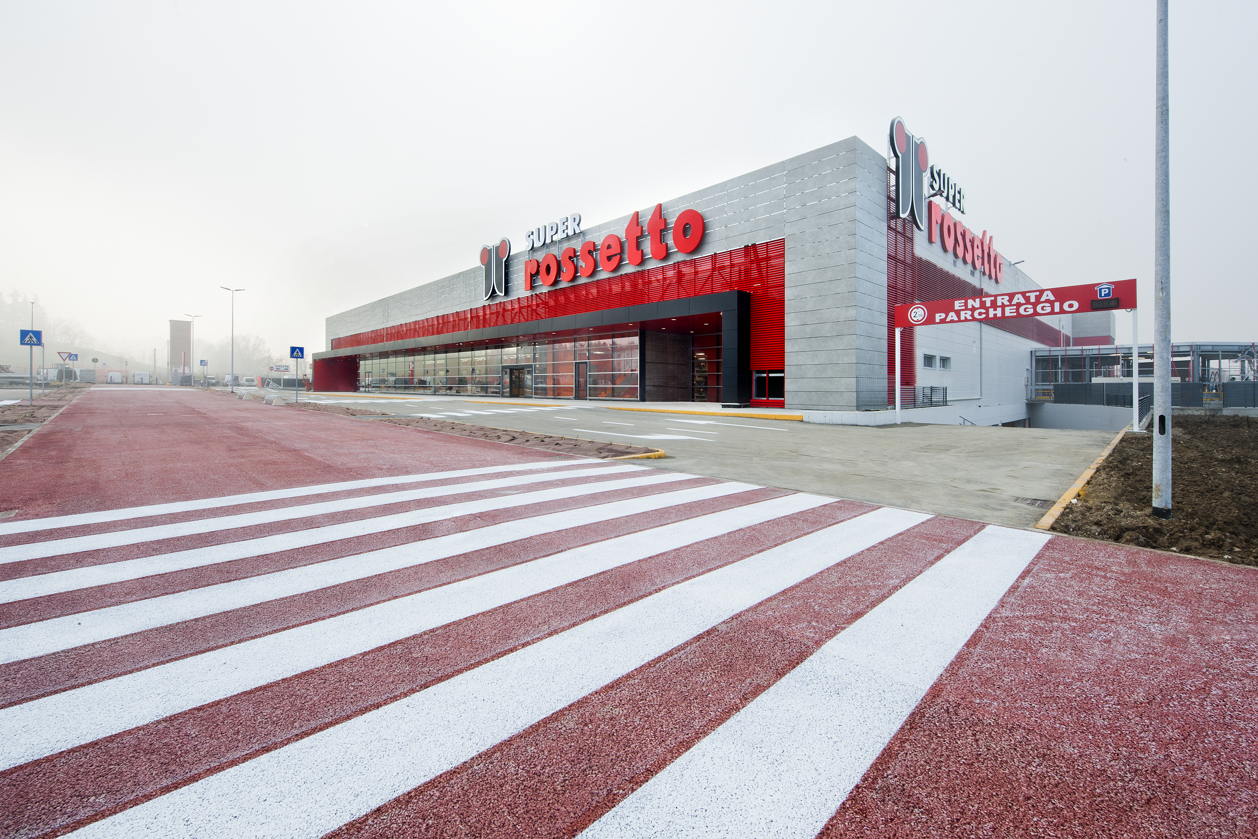 Red outdoor tiles on the forecourt of a modern commercial building with a zebra crossing.