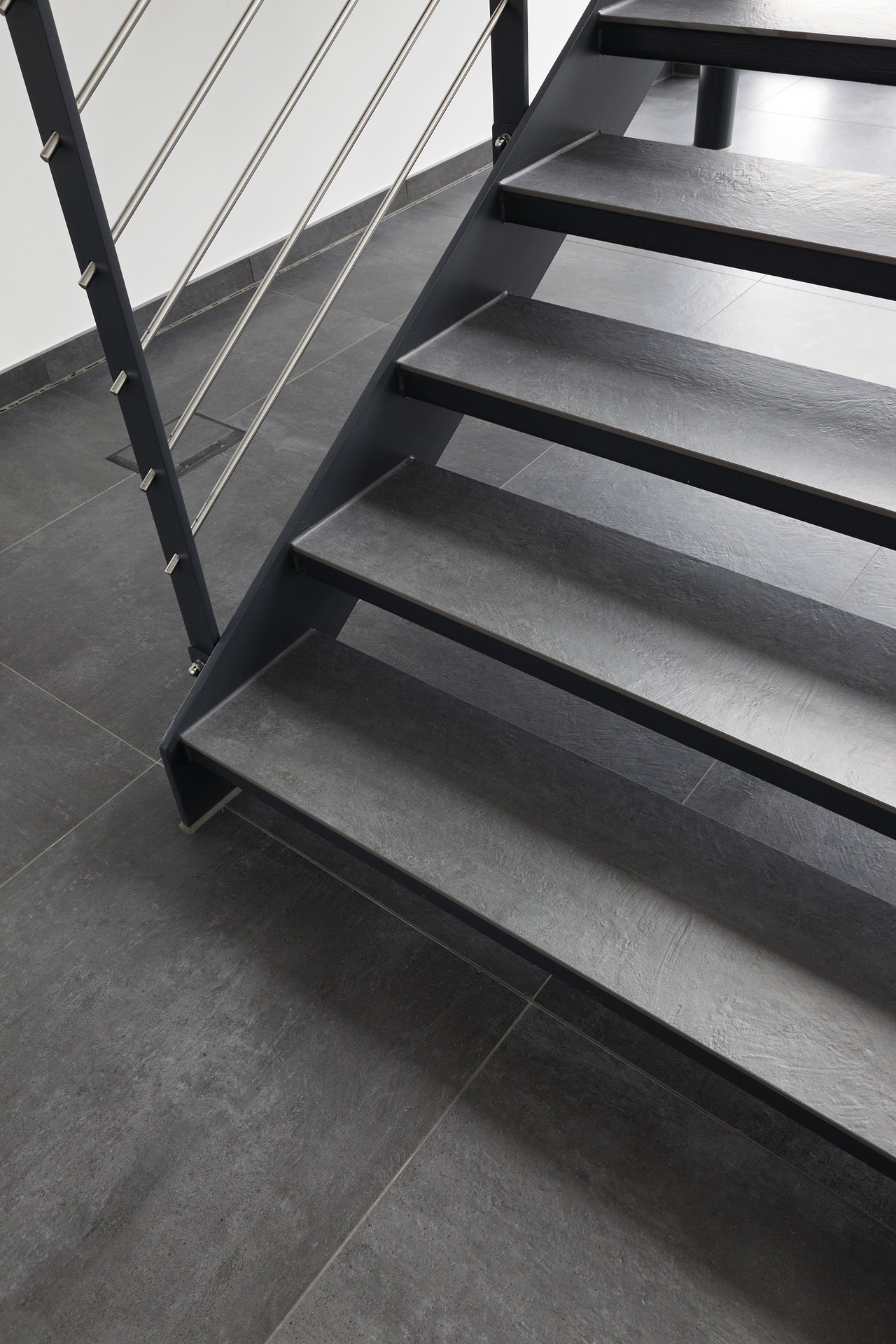 Modern staircase with dark grey tile steps and matching floor.