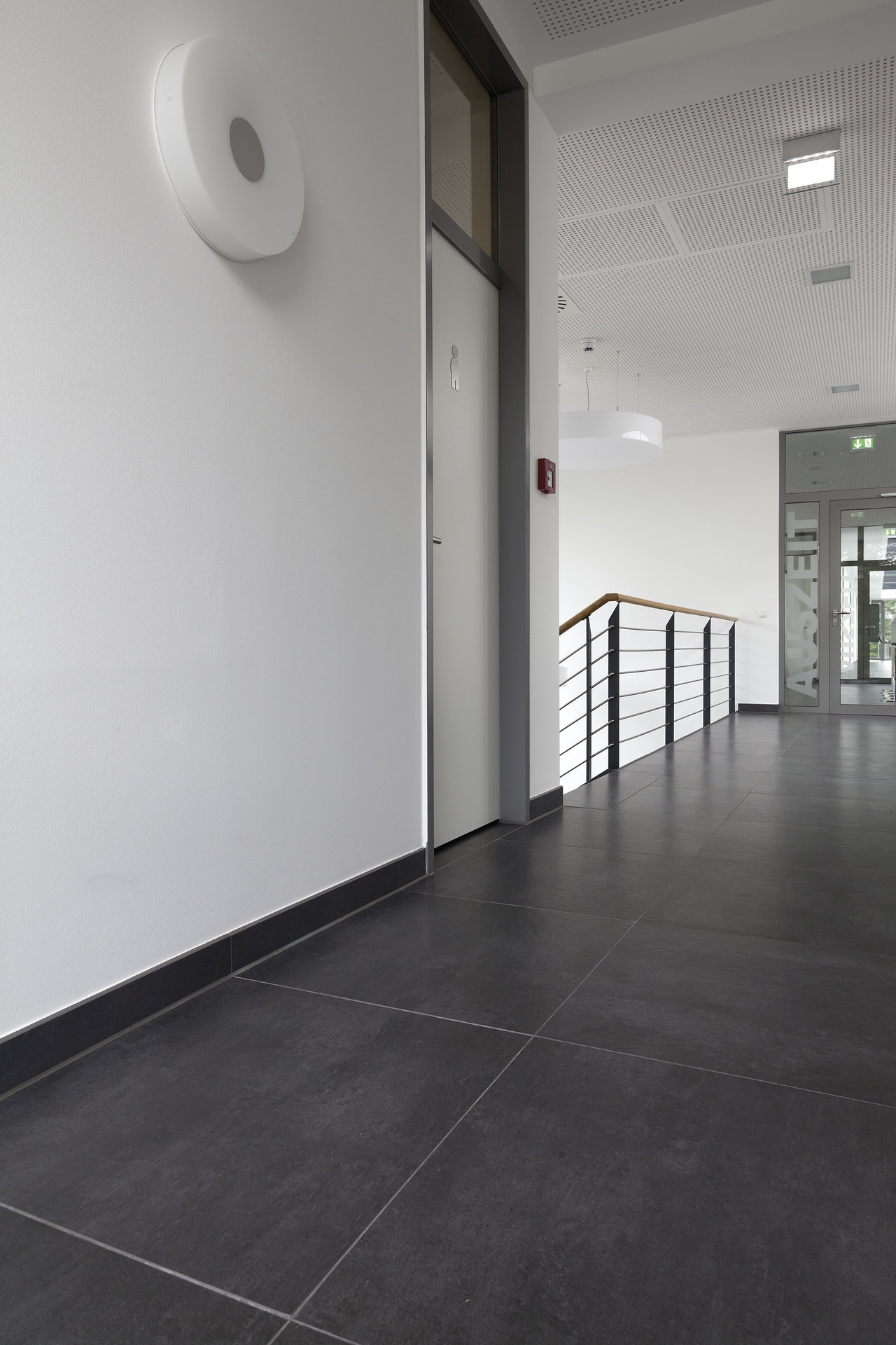 Modern hallway with dark, large-format floor tiles and matching skirting boards.