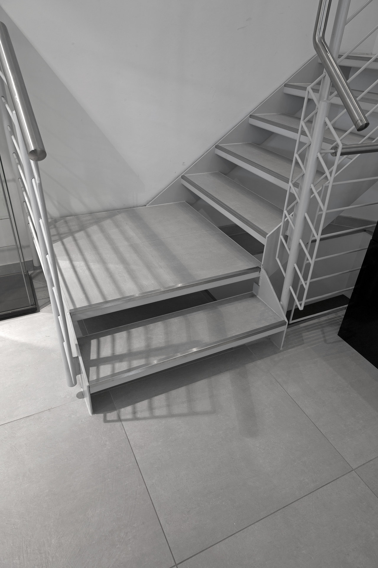 Large-format, light-grey tiles under a modern staircase.