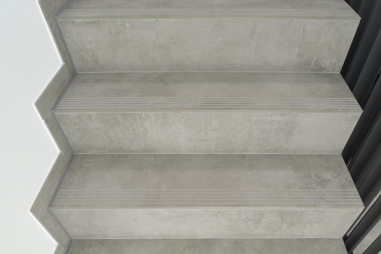 Porcelaingres concrete-look stair tiles with anti-slip grooves.