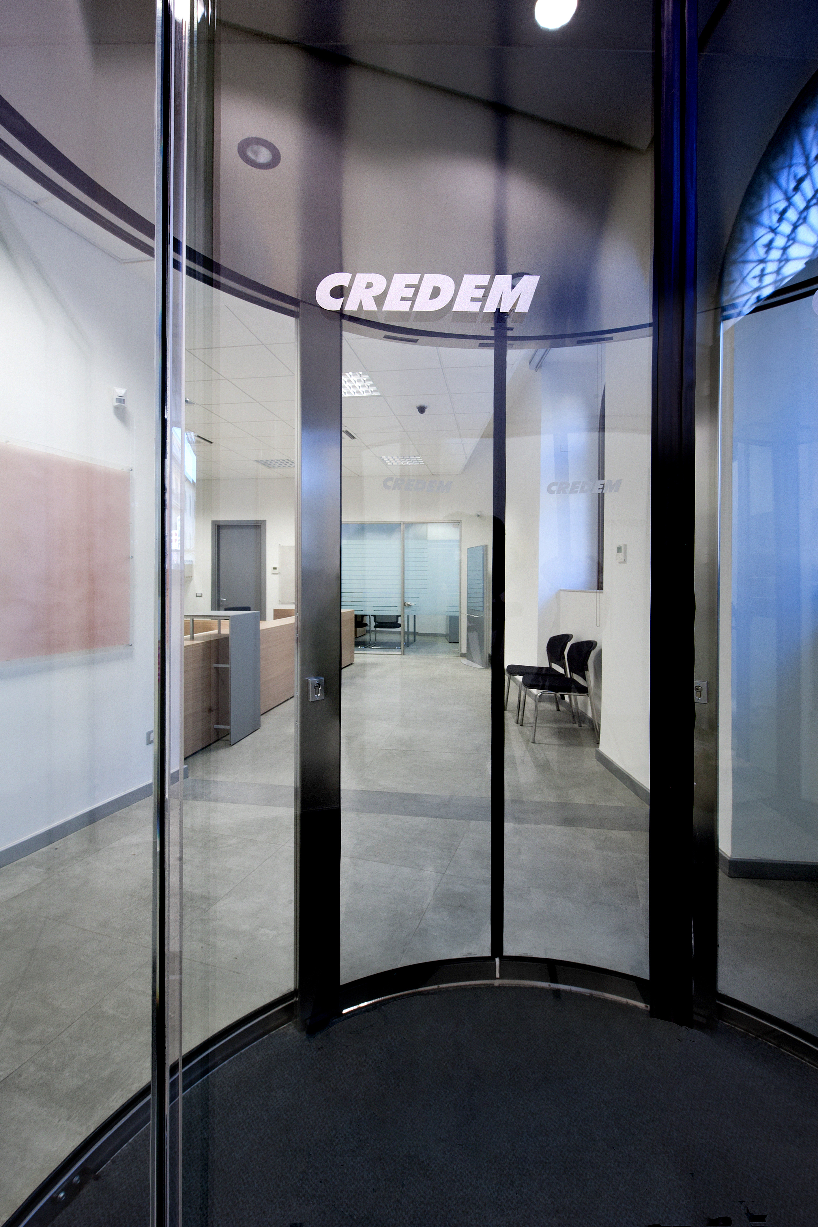 Bright reception area with glass pivot door and large-format floor tiles.