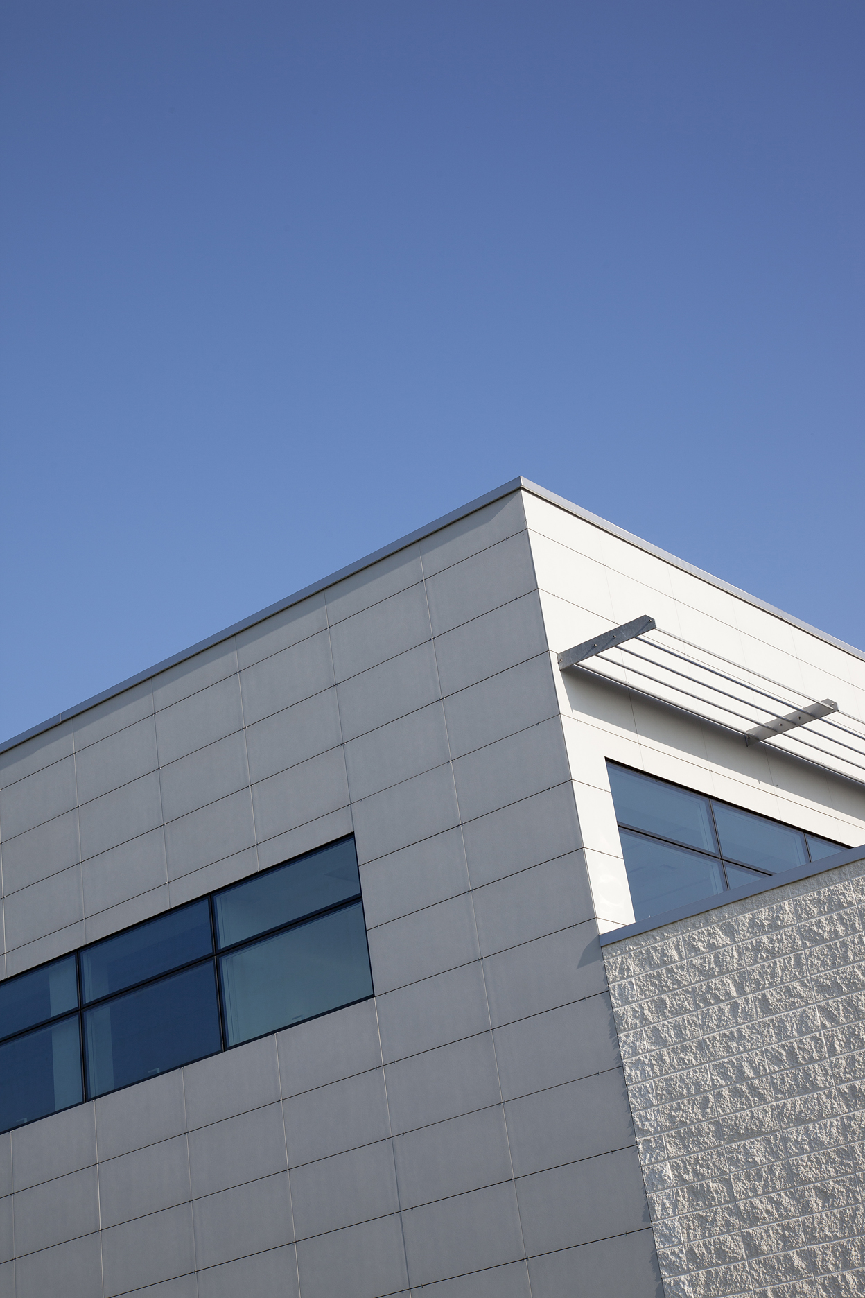 Modern building facade with smooth and textured tiles under a blue sky.