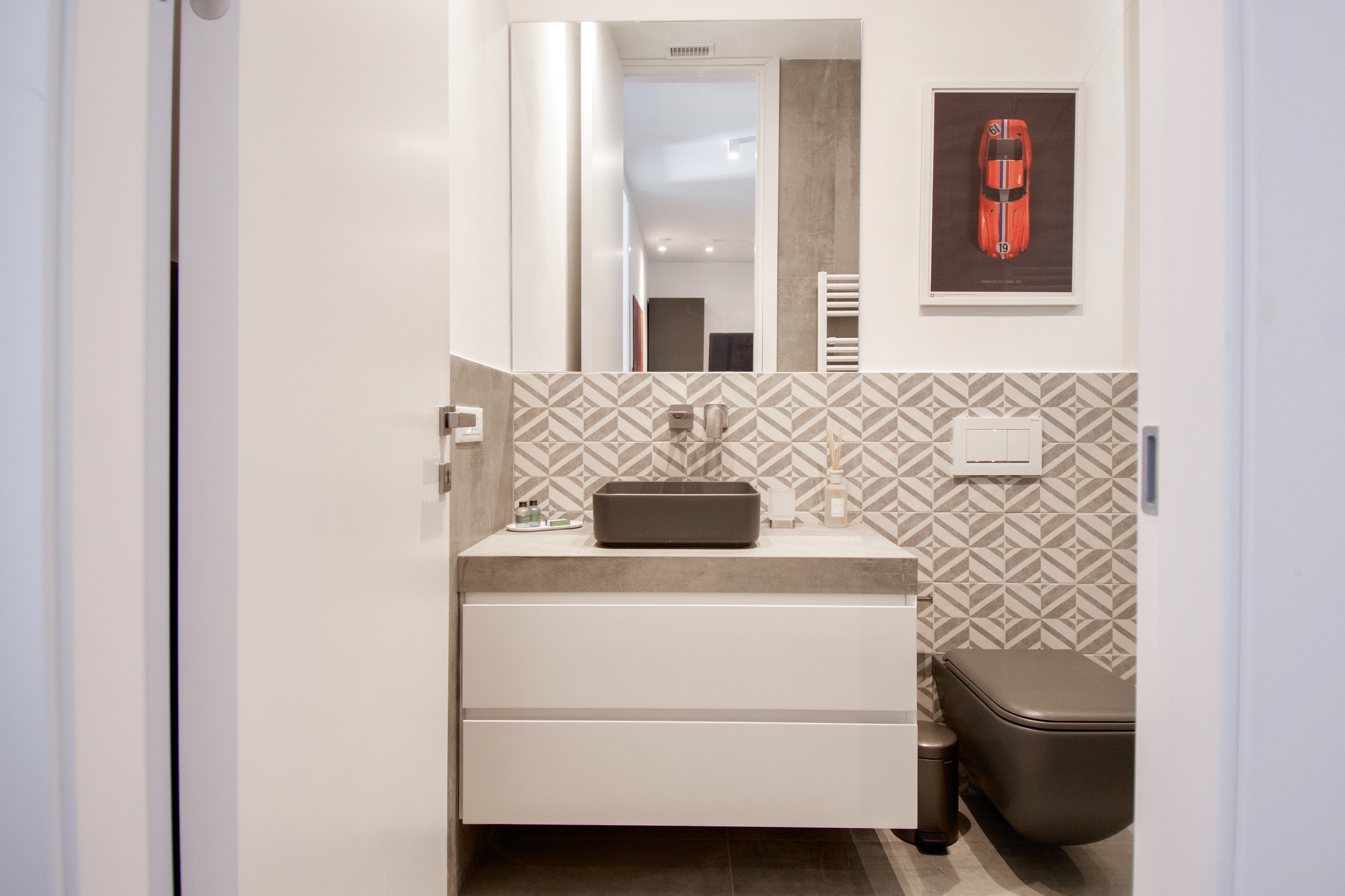 Modern guest WC with elegant grey patterned tiles, dark vanity and floating toilet.