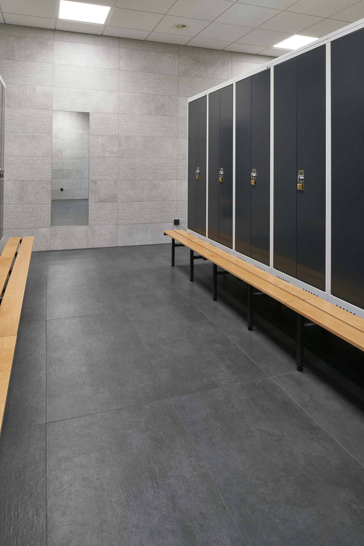 Modern changing room with dark floor tiles and light grey wall tiles.