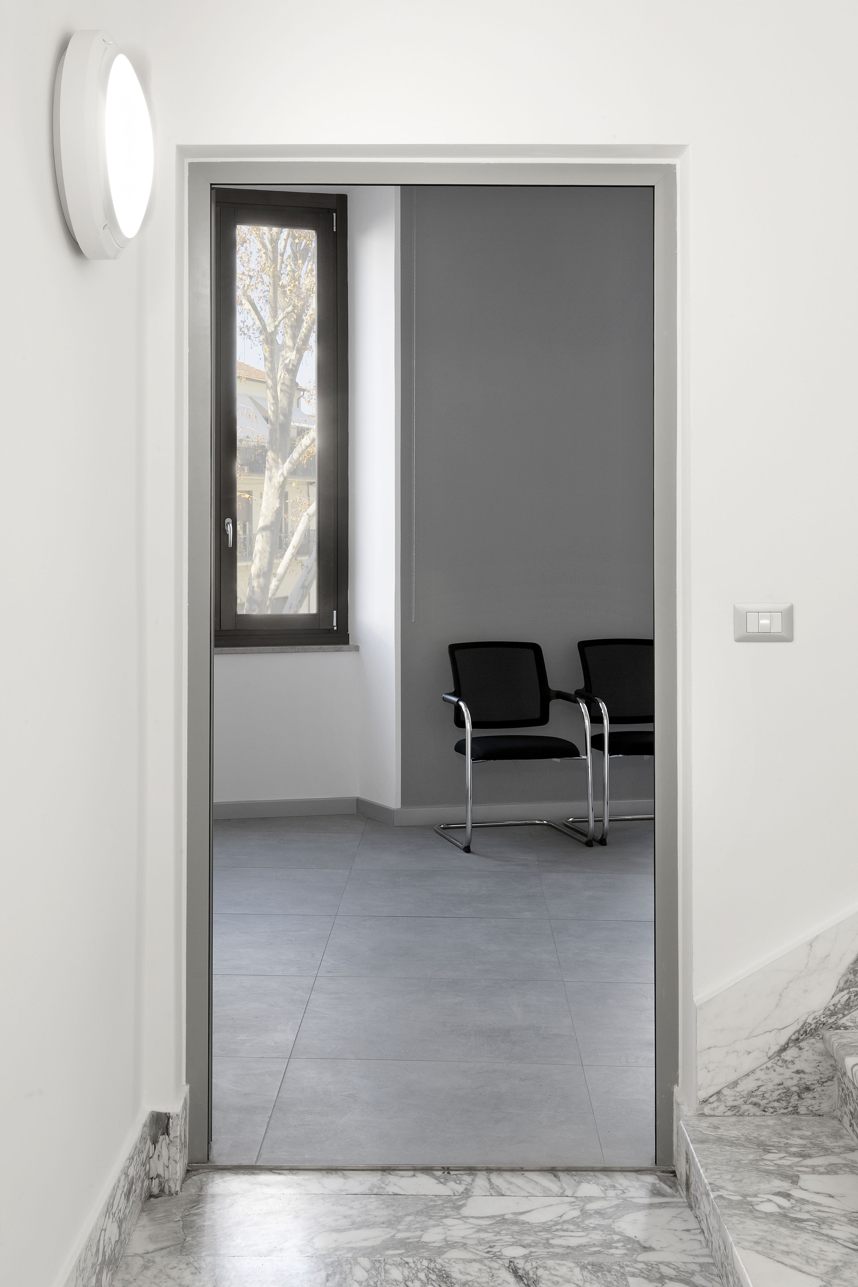 Indoor grey porcelain tiles, visible through a door frame in a waiting room.