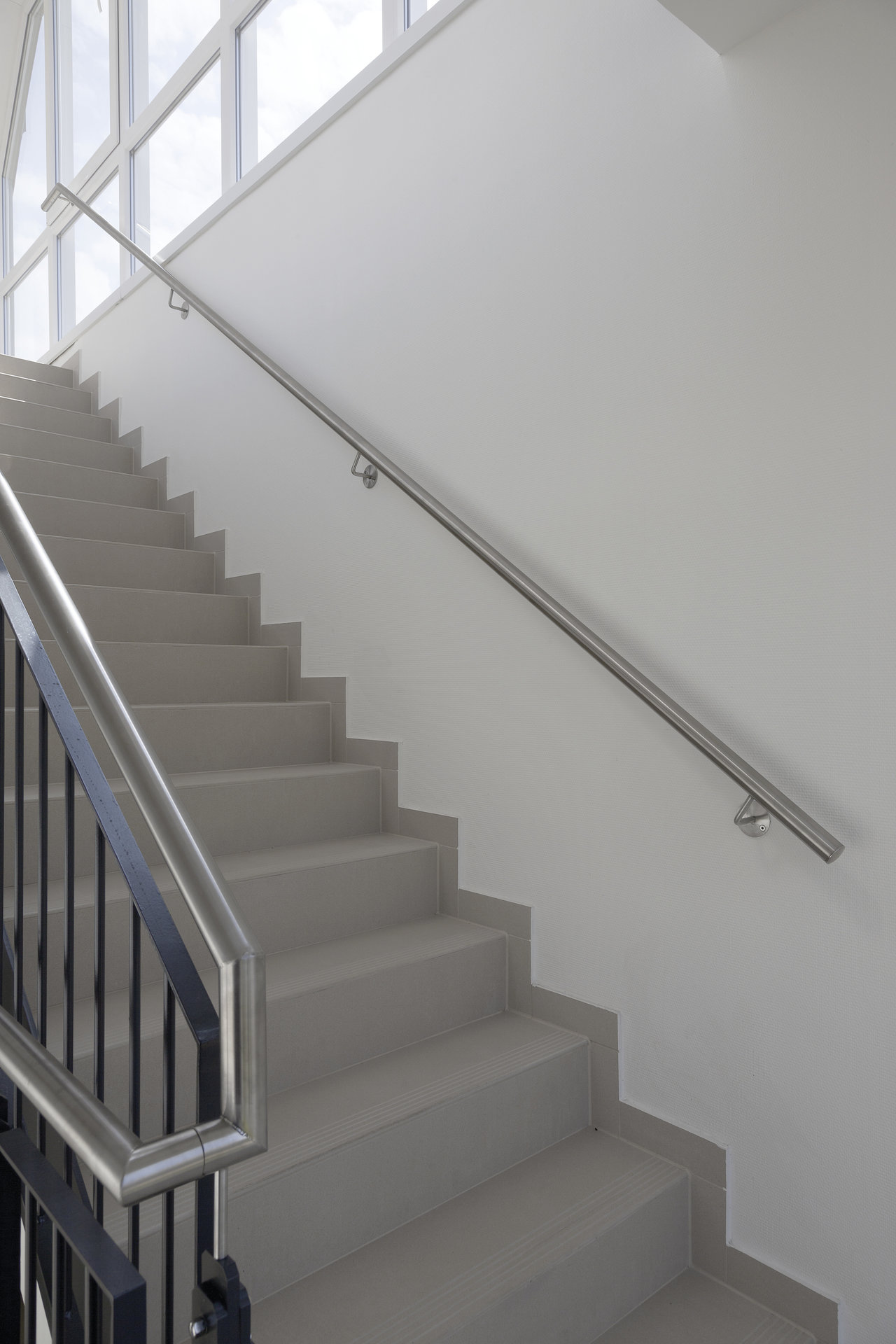 Modern indoor staircase with grey tiles and stainless steel railing.
