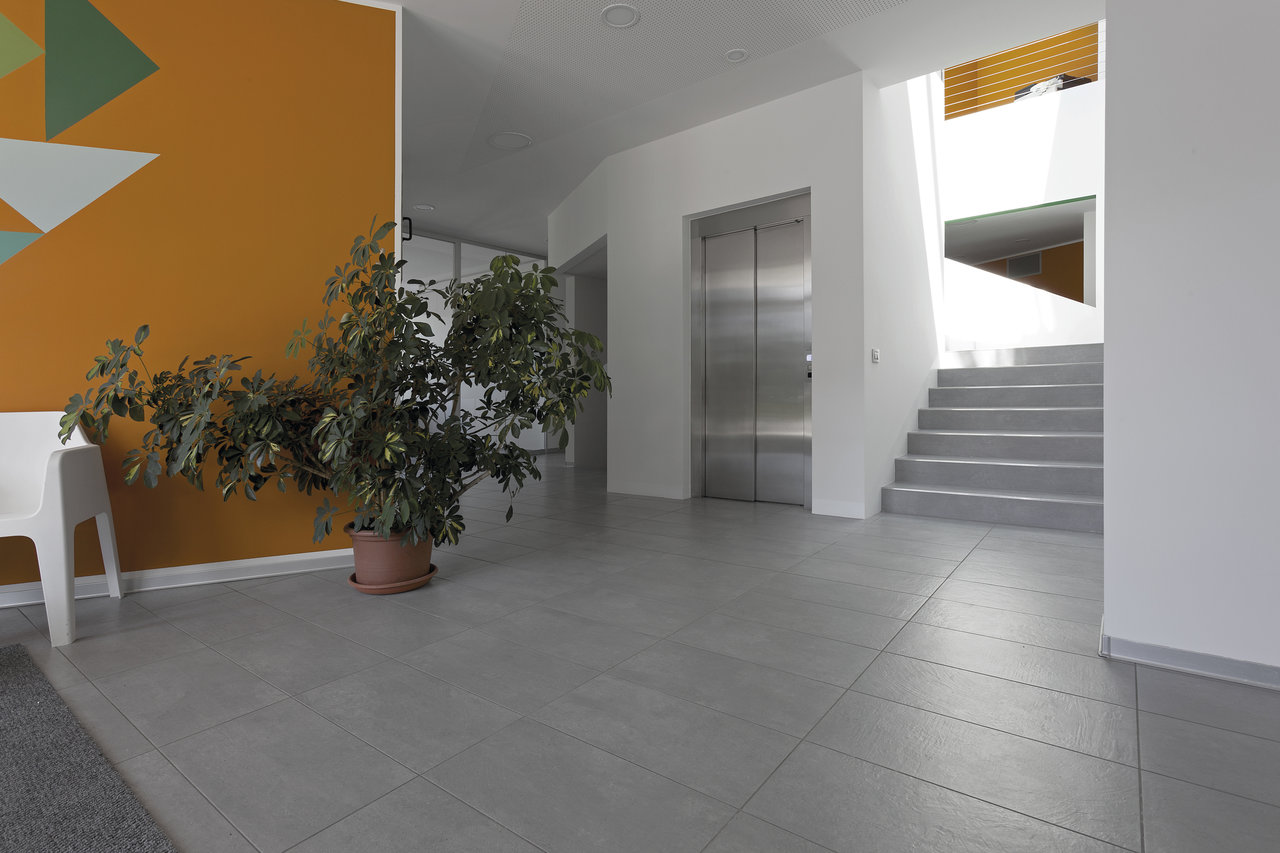 Modern hallway with light grey floor tiles, lift and stairs.