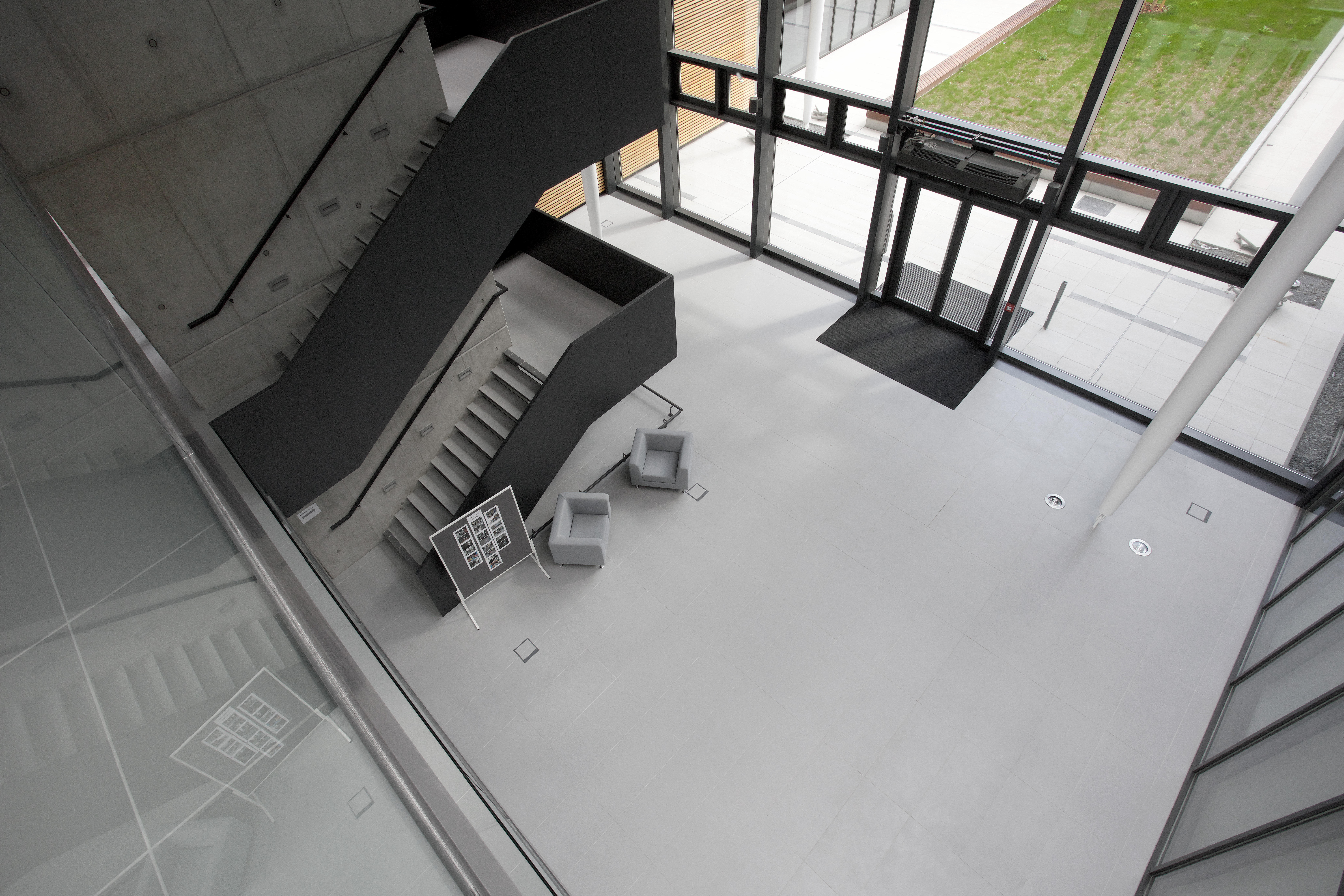 Modern entrance area with light grey tiles, dark stairs and seating.