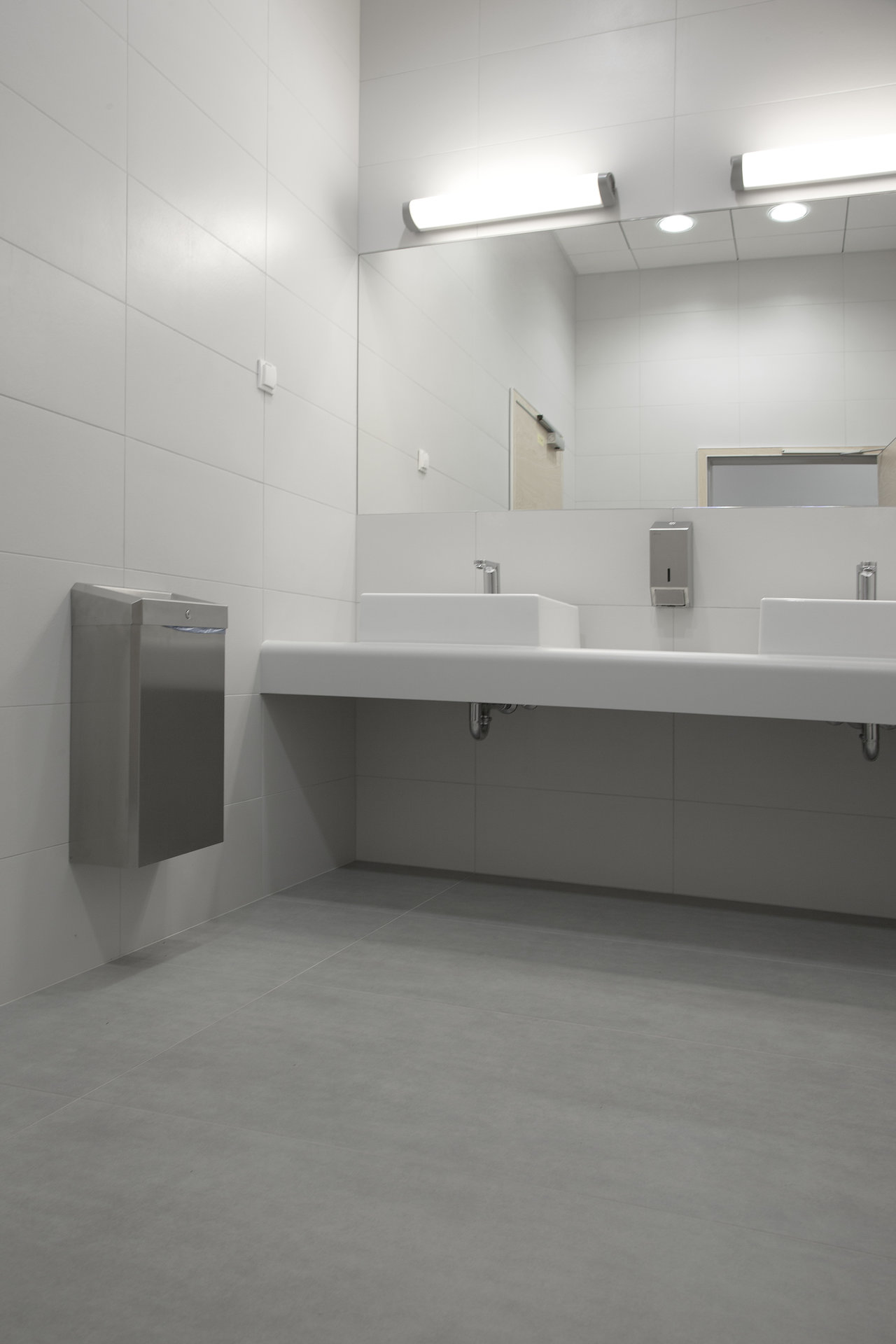 Modern bathroom with white wall and grey floor tiles.