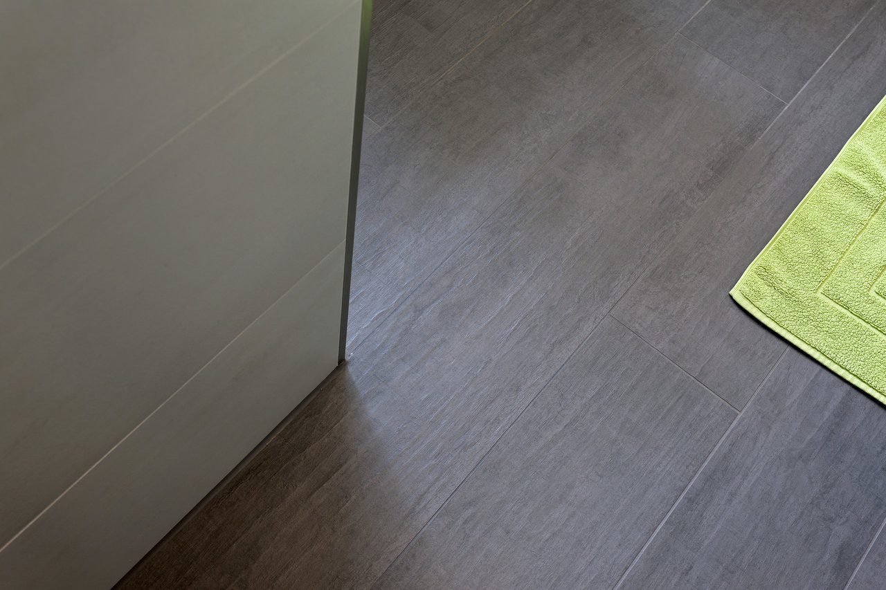 Dark floor tiles in wood plank format with green bath mat.