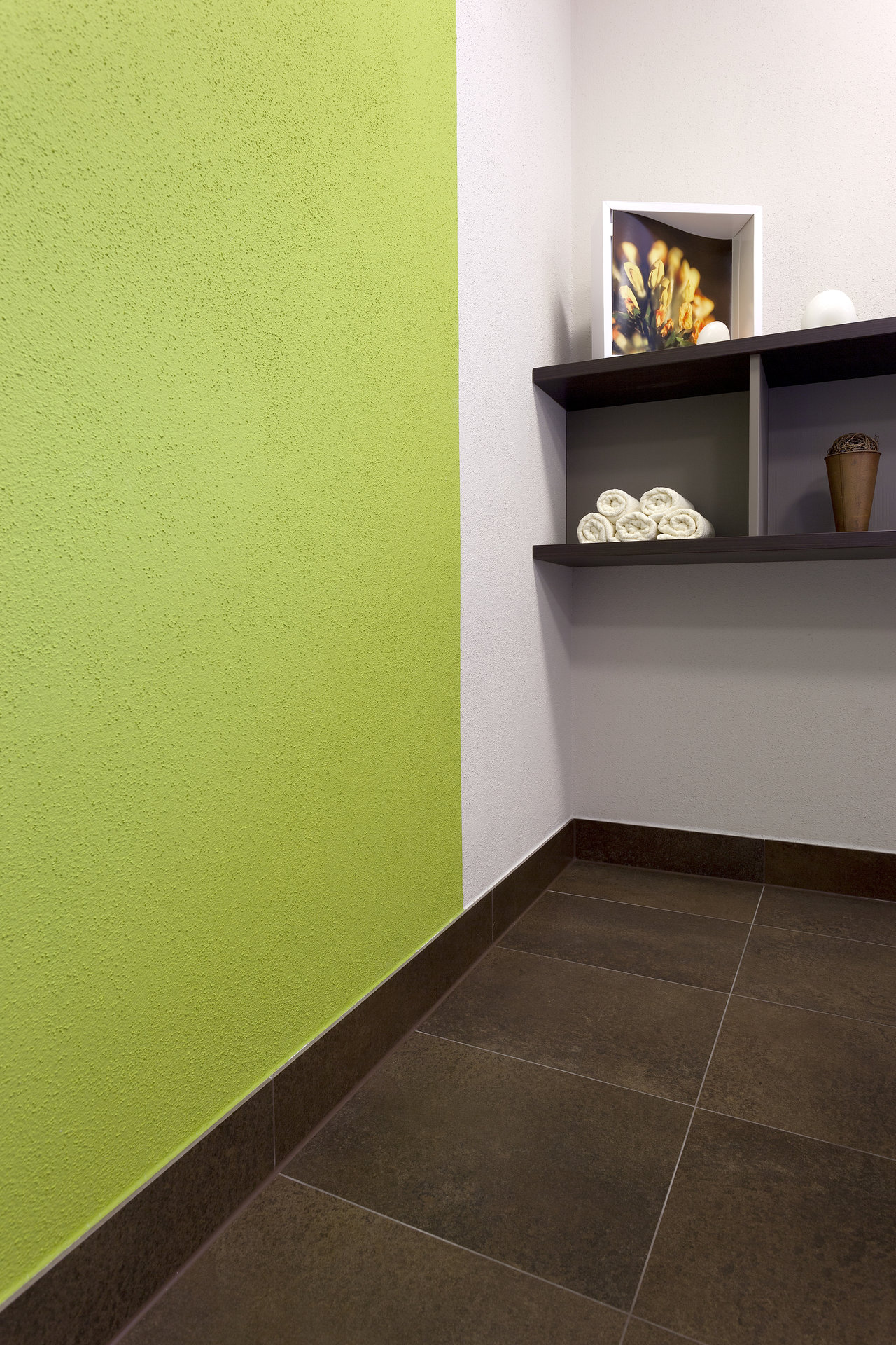 Dark brown floor tiles and skirting boards in a modern room with a green wall.