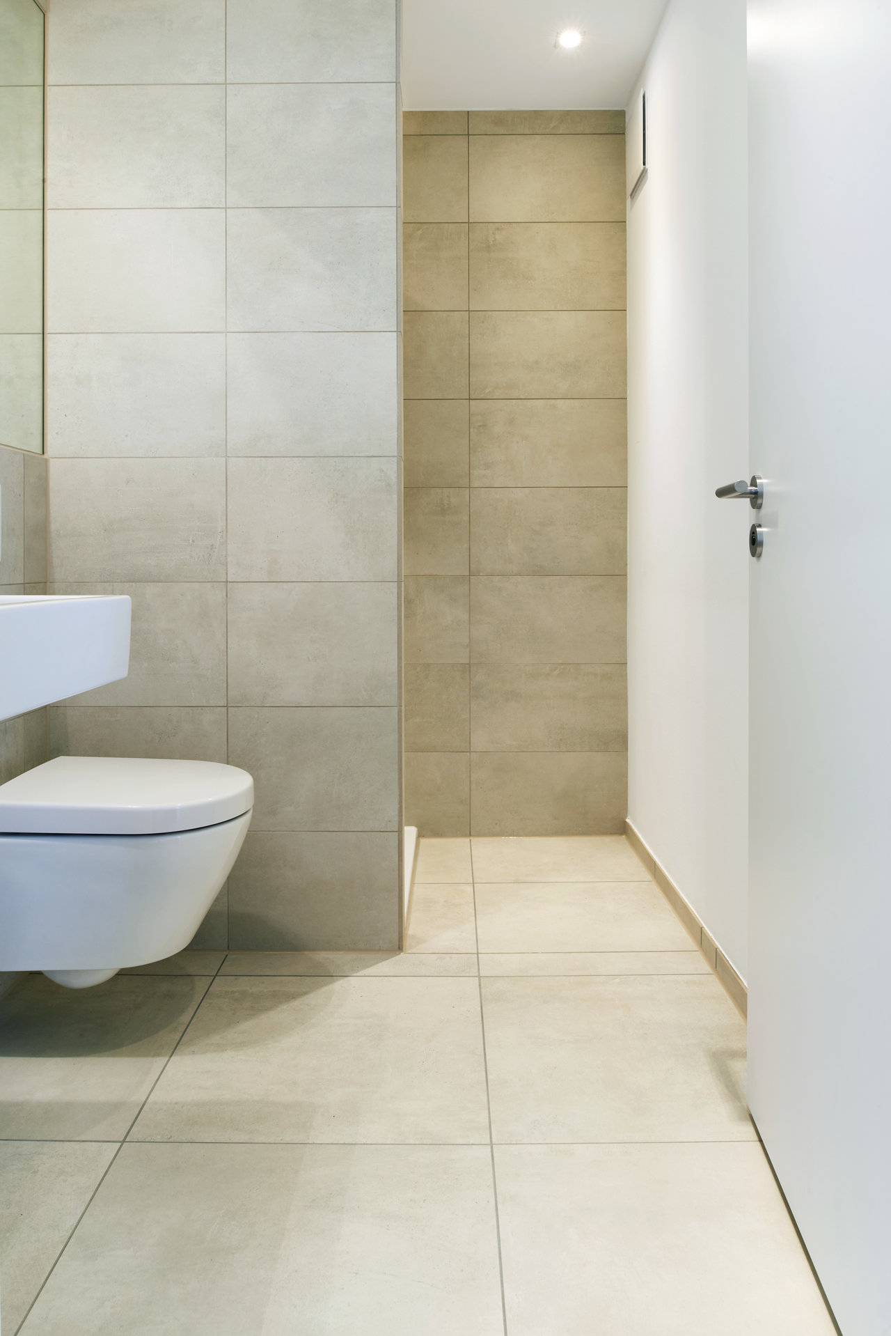 Modern bathroom with light, large-format wall and floor tiles.