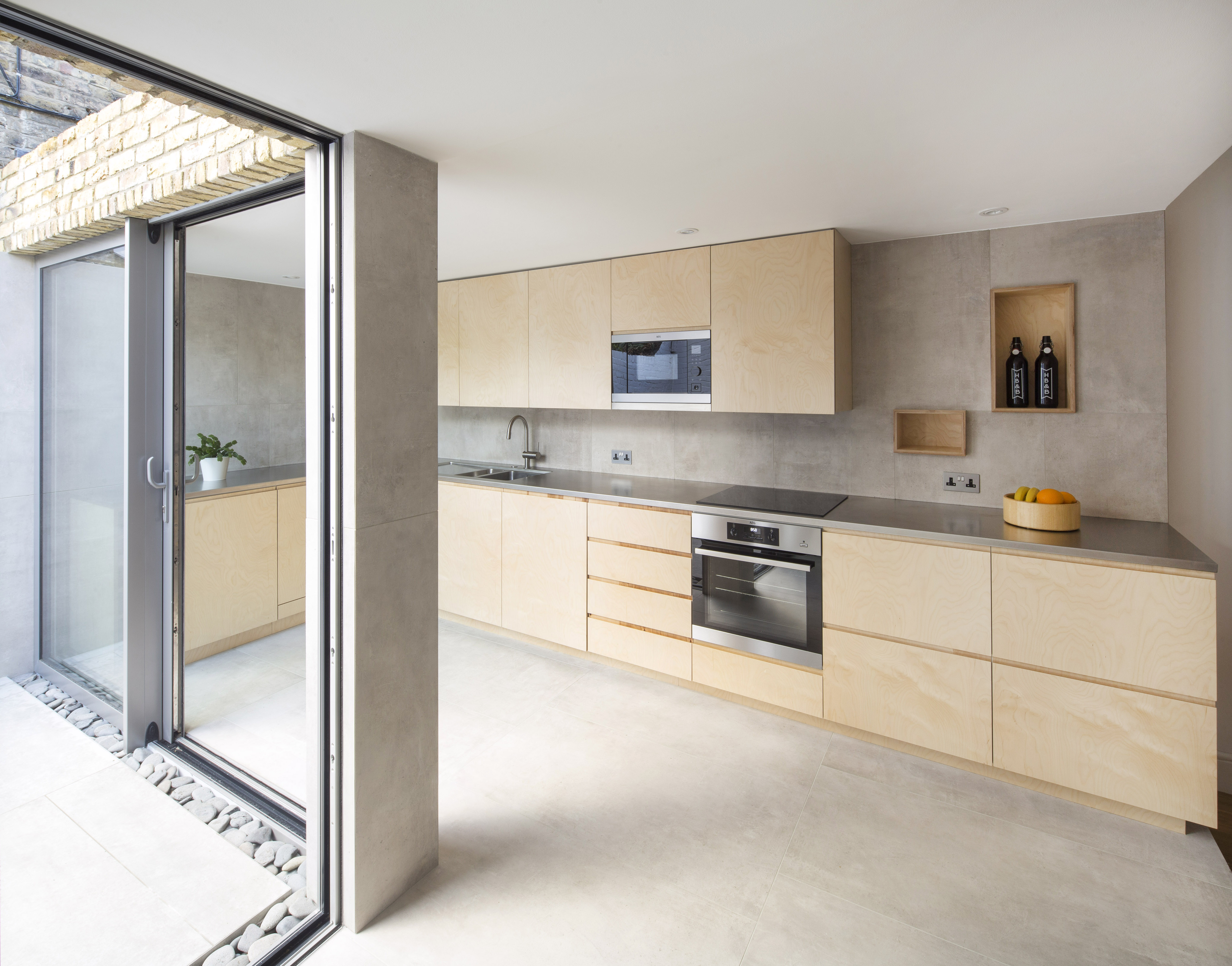 Modern kitchen with grey concrete-effect tiles, light wood, and open outdoor access.