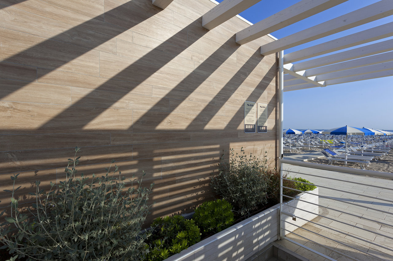 Light outdoor wall tiles, pergola-shaded, with a beach view.