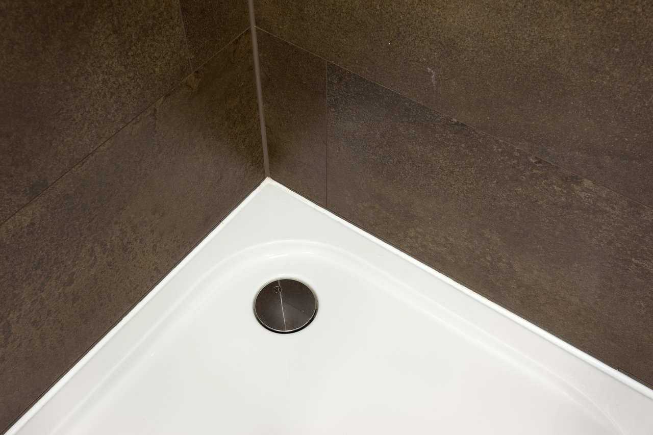 Dark brown natural stone look tiles in shower with white shower tray.