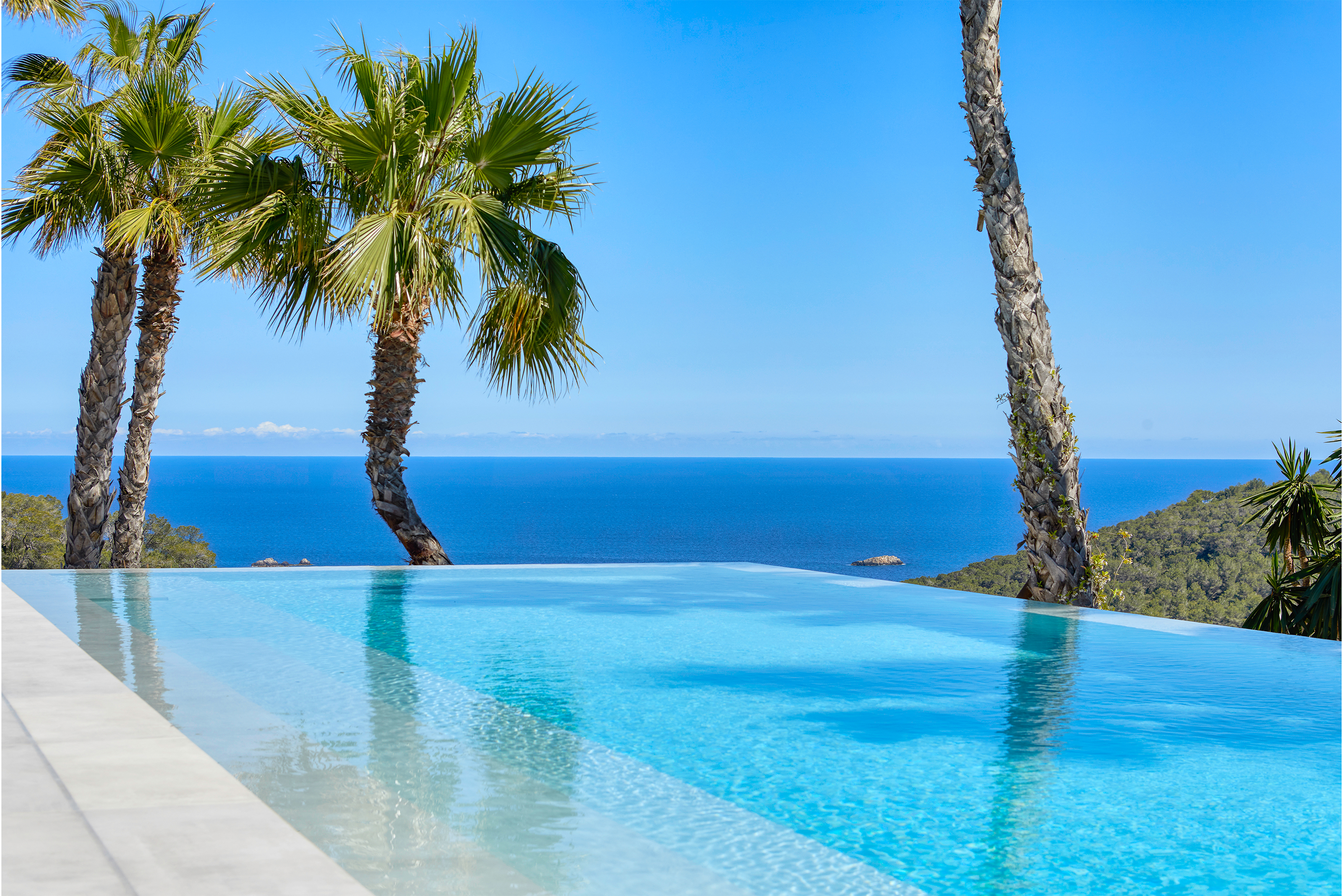Exclusive infinity pool with light outdoor tiles, sea view, and palm trees.