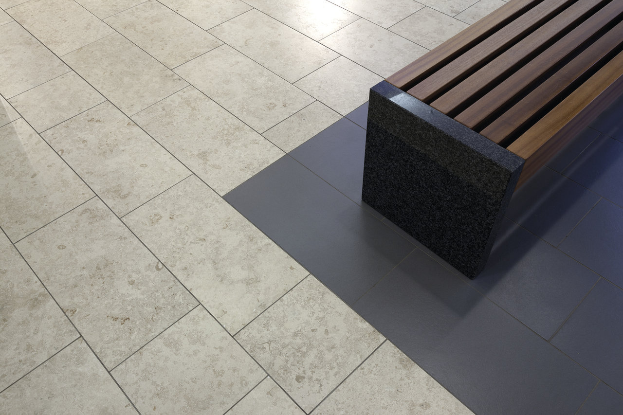 Light, rectangular floor tiles with a dark accent area under a modern bench.