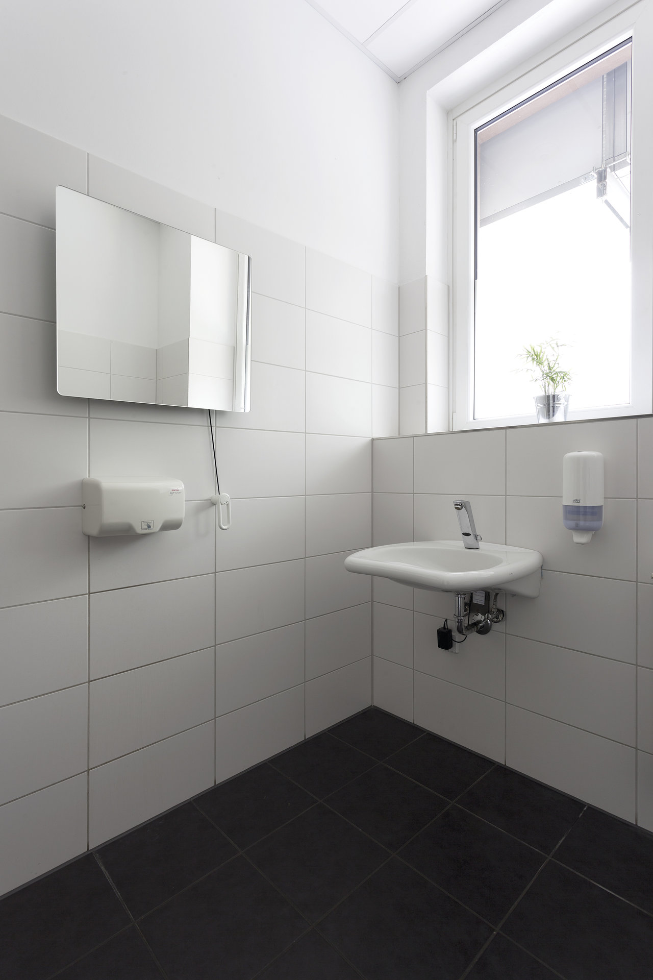 Modern tiled washroom with white wall and dark floor tiles.