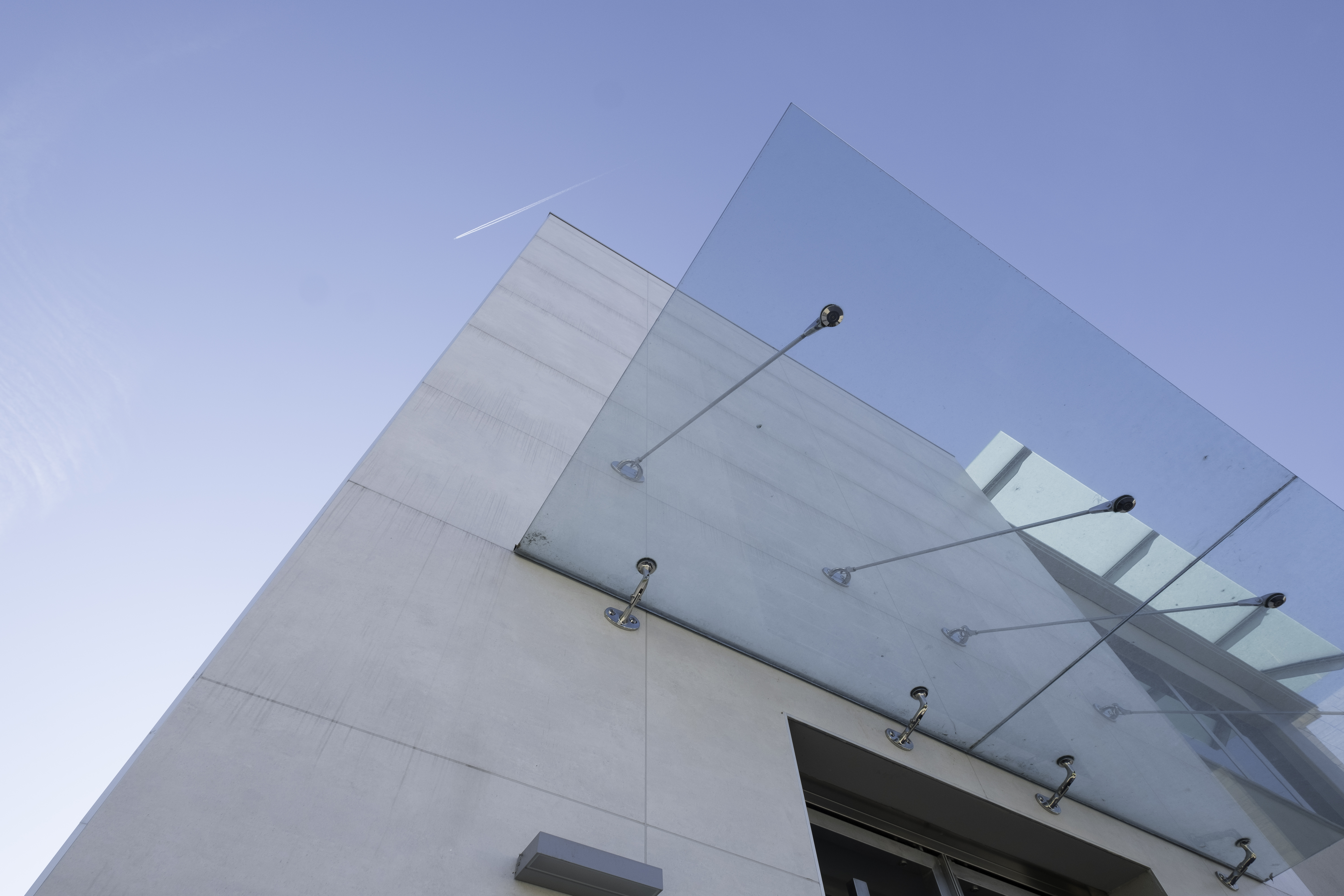 Modern building facade with large glass canopy against a blue sky.