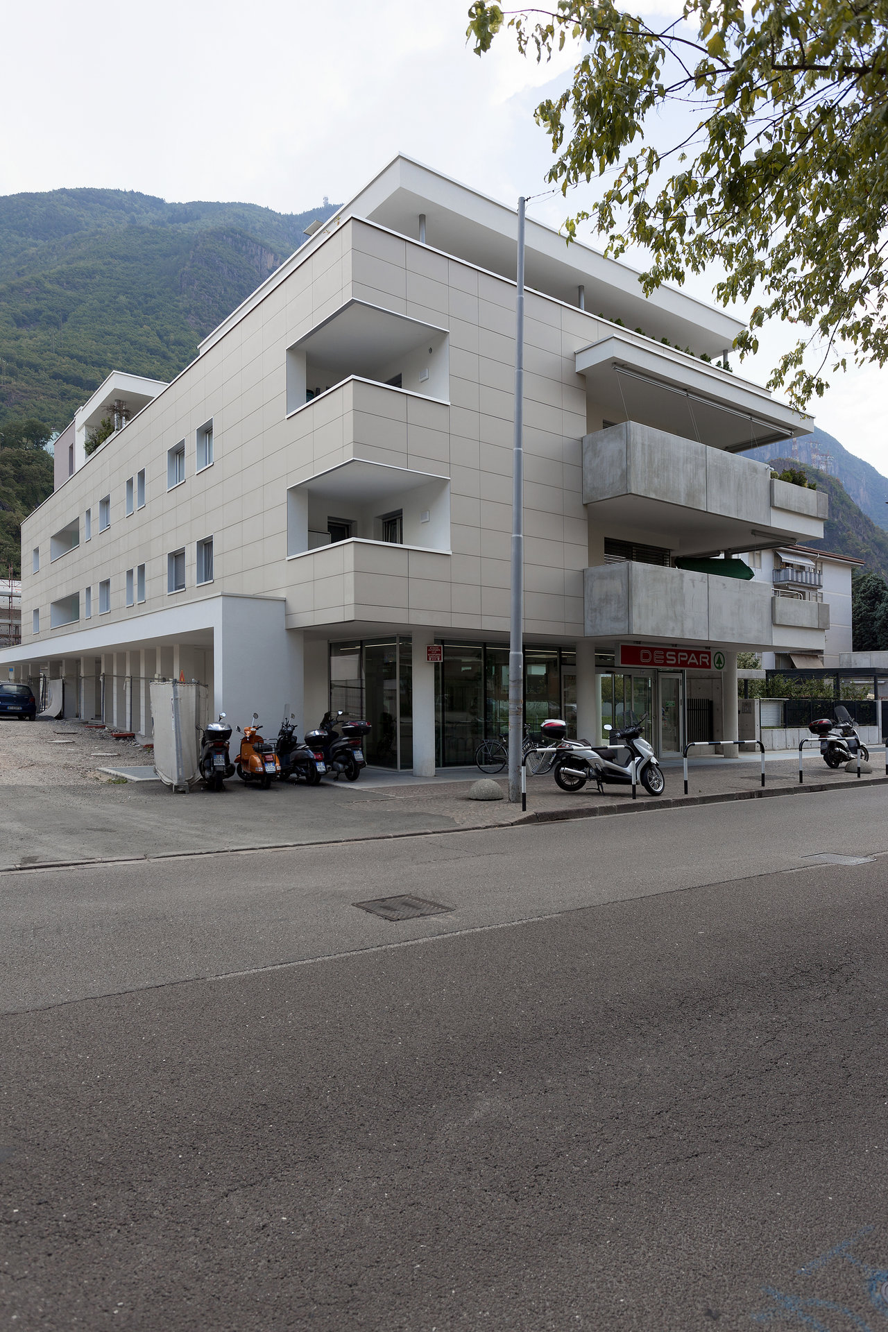 Modern building with light tile cladding and balconies against a mountain backdrop.