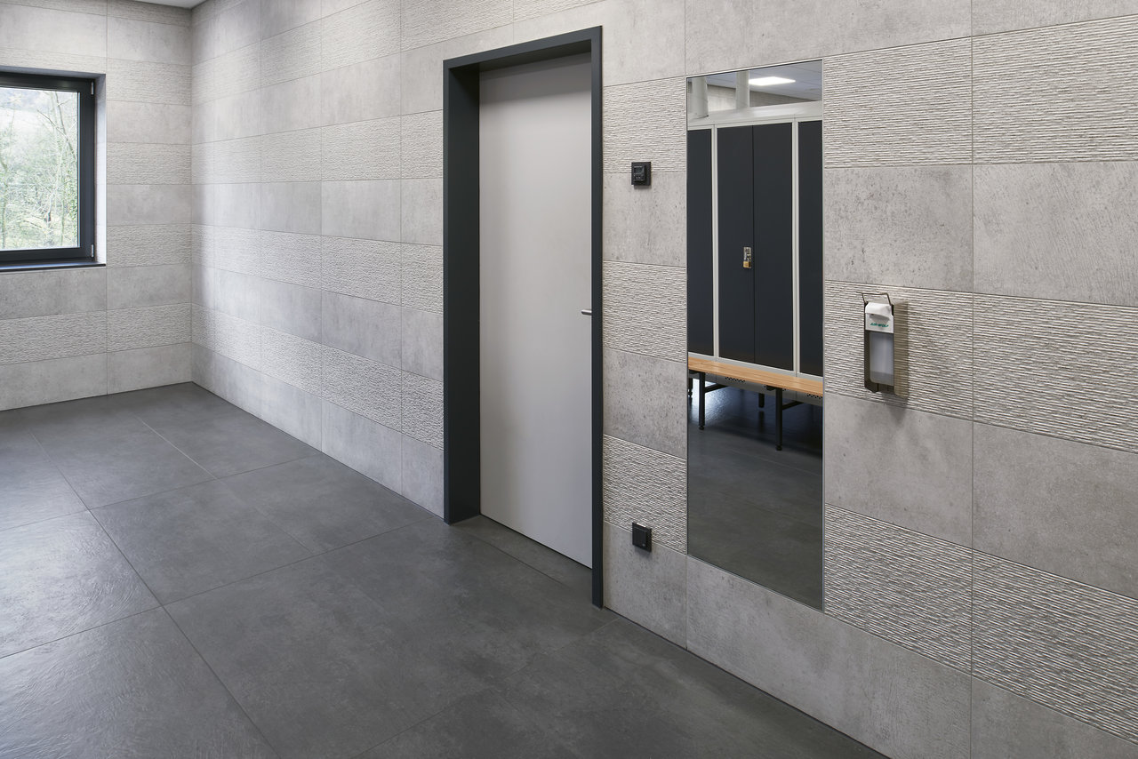 Modern changing room with textured light grey wall tiles and dark grey floor tiles.