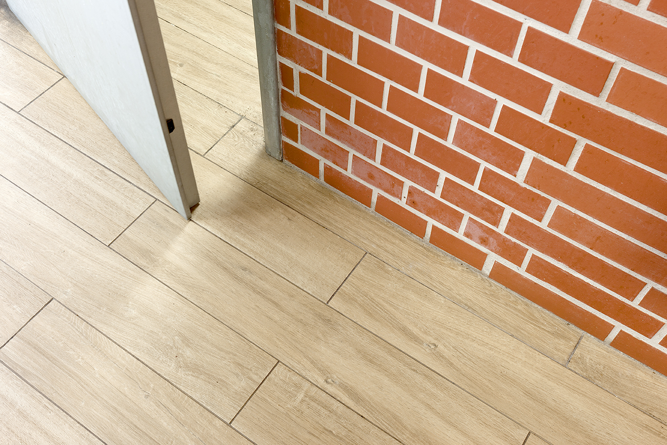 Light wood effect floor tiles in front of a decorative brick wall.