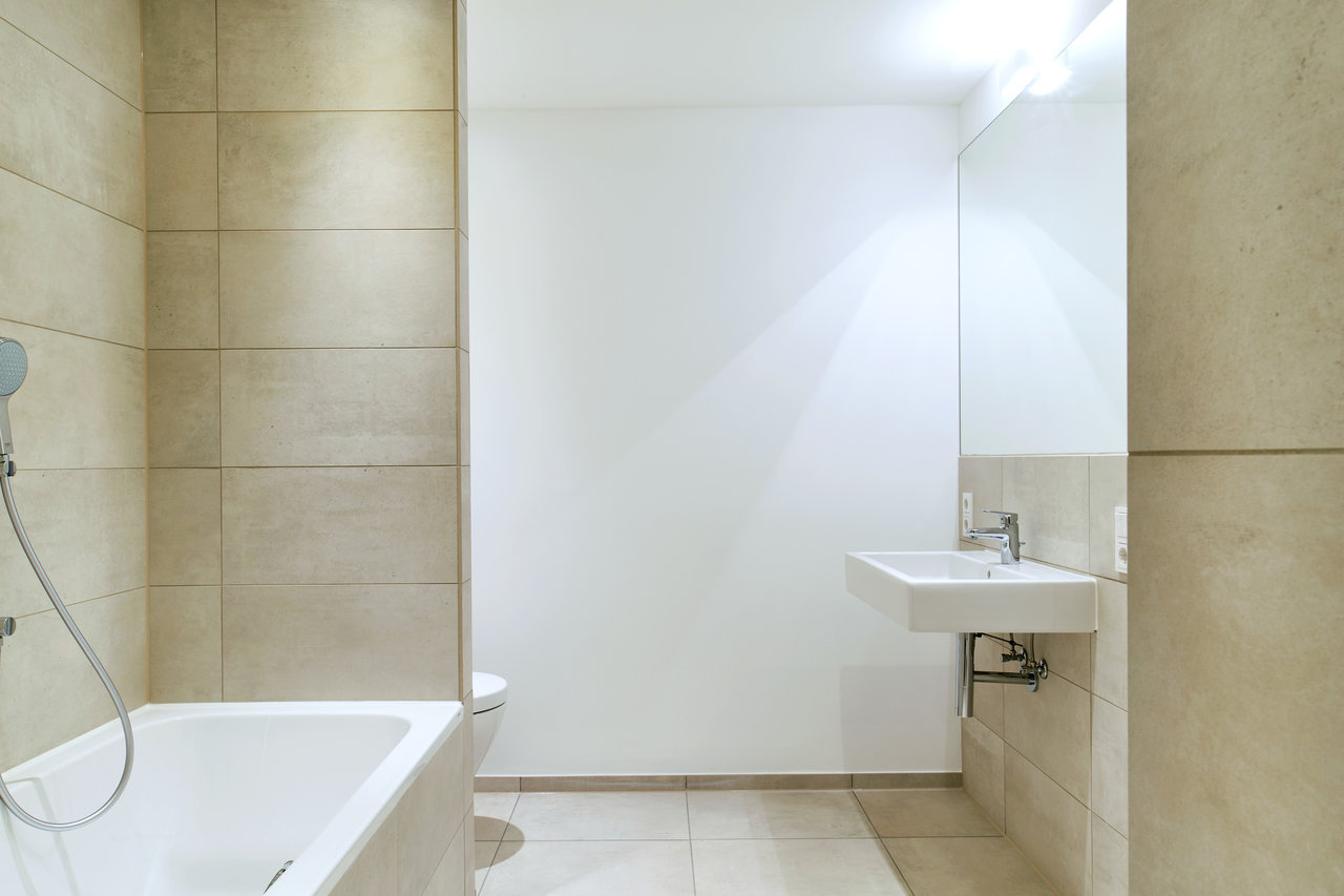 High-quality bathroom with beige wall and floor tiles, bathtub, and washbasin.