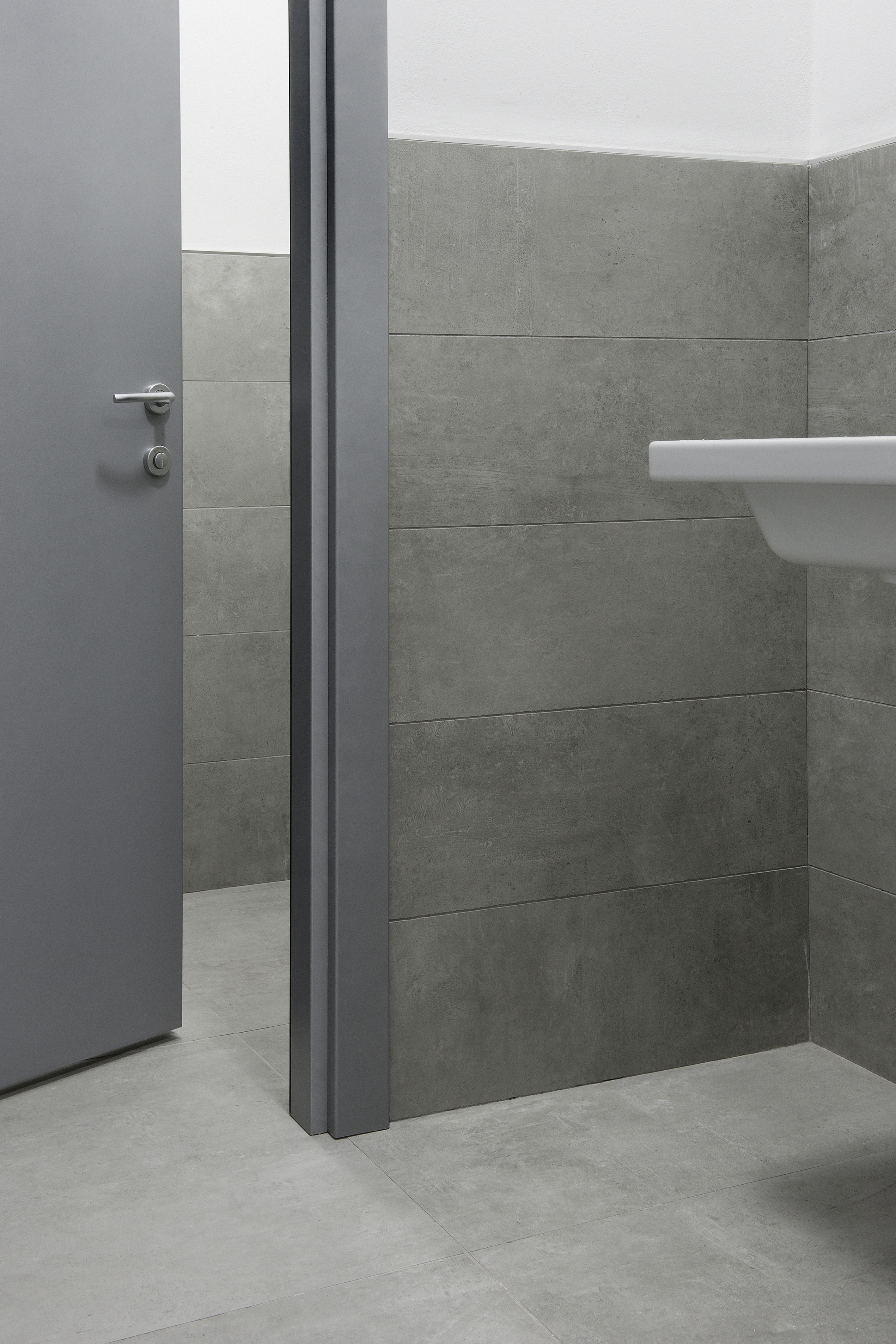 Grey porcelain stoneware tiles on wall and floor in a minimalist bathroom with a washbasin.