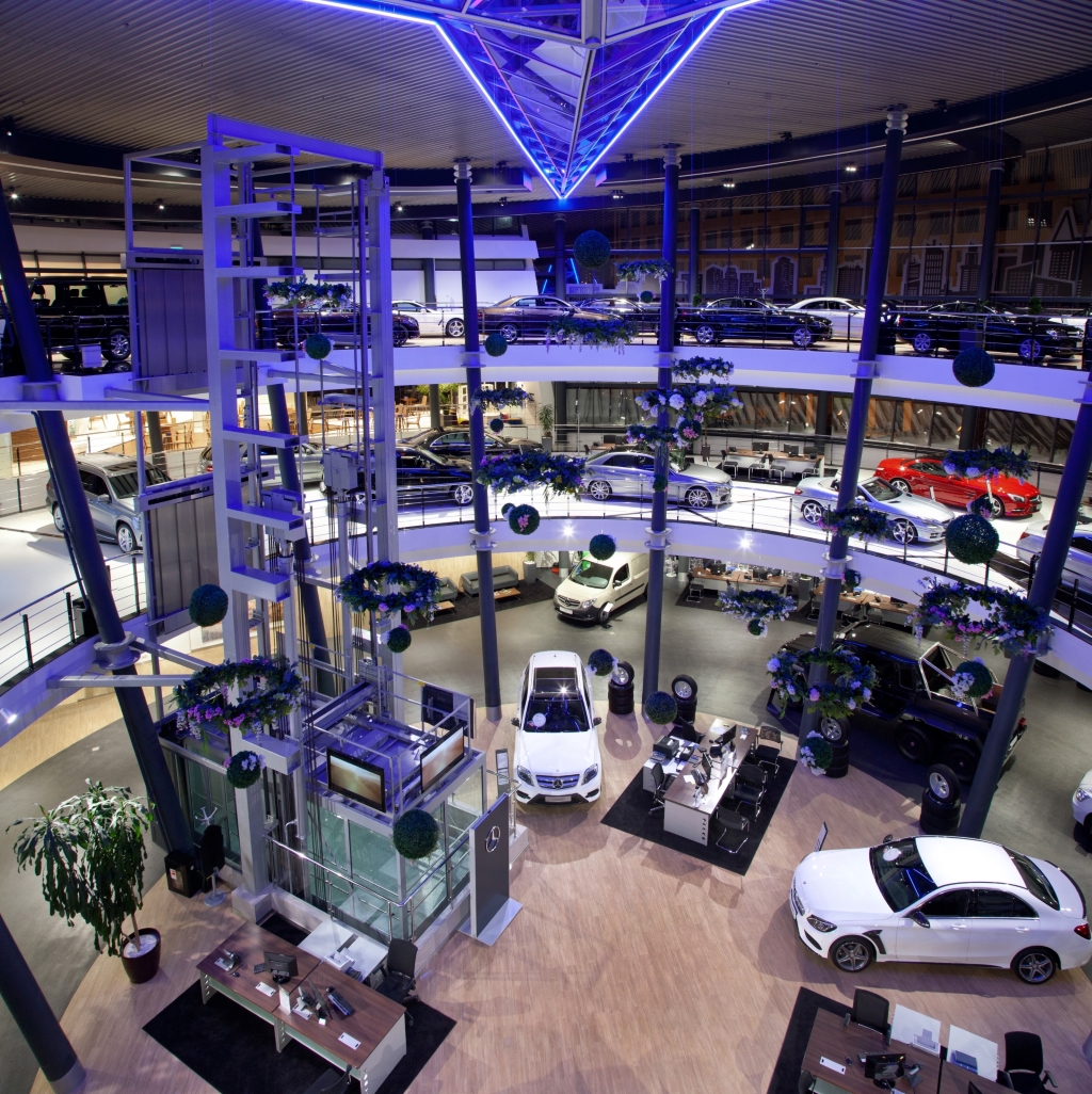 Modern, multi-story car showroom with blue lighting and many cars.
