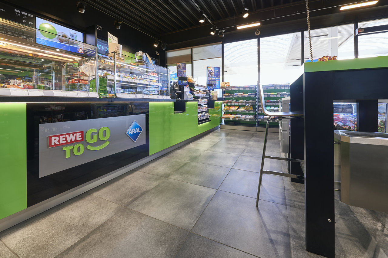 Grey, large-format floor tiles in a REWE To Go shop, an example of robust indoor tiles.