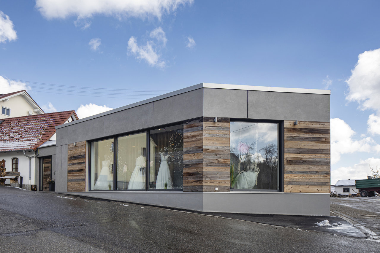 Modern building with grey facade and wood cladding, wedding dresses visible in the shop windows.