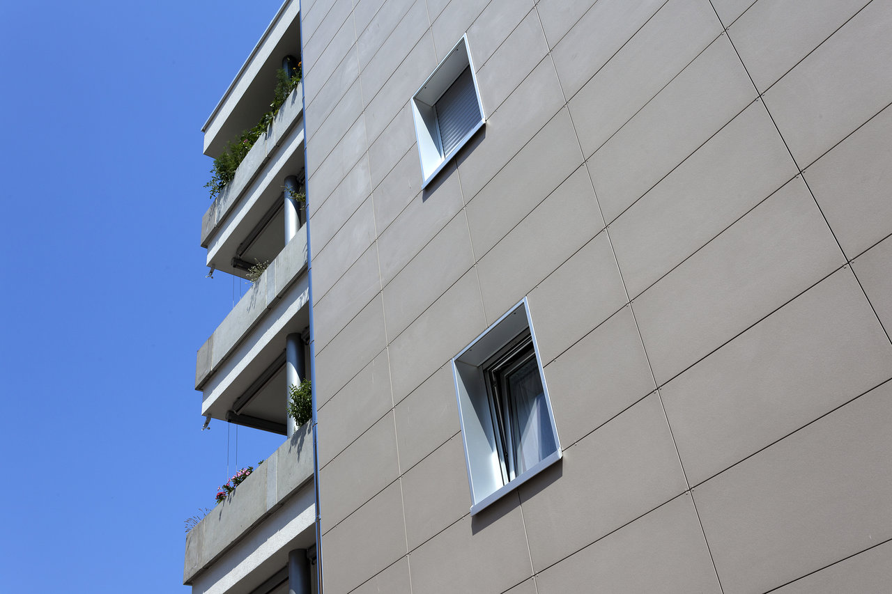Modern building facade with large-format outdoor tiles and windows under a blue sky.