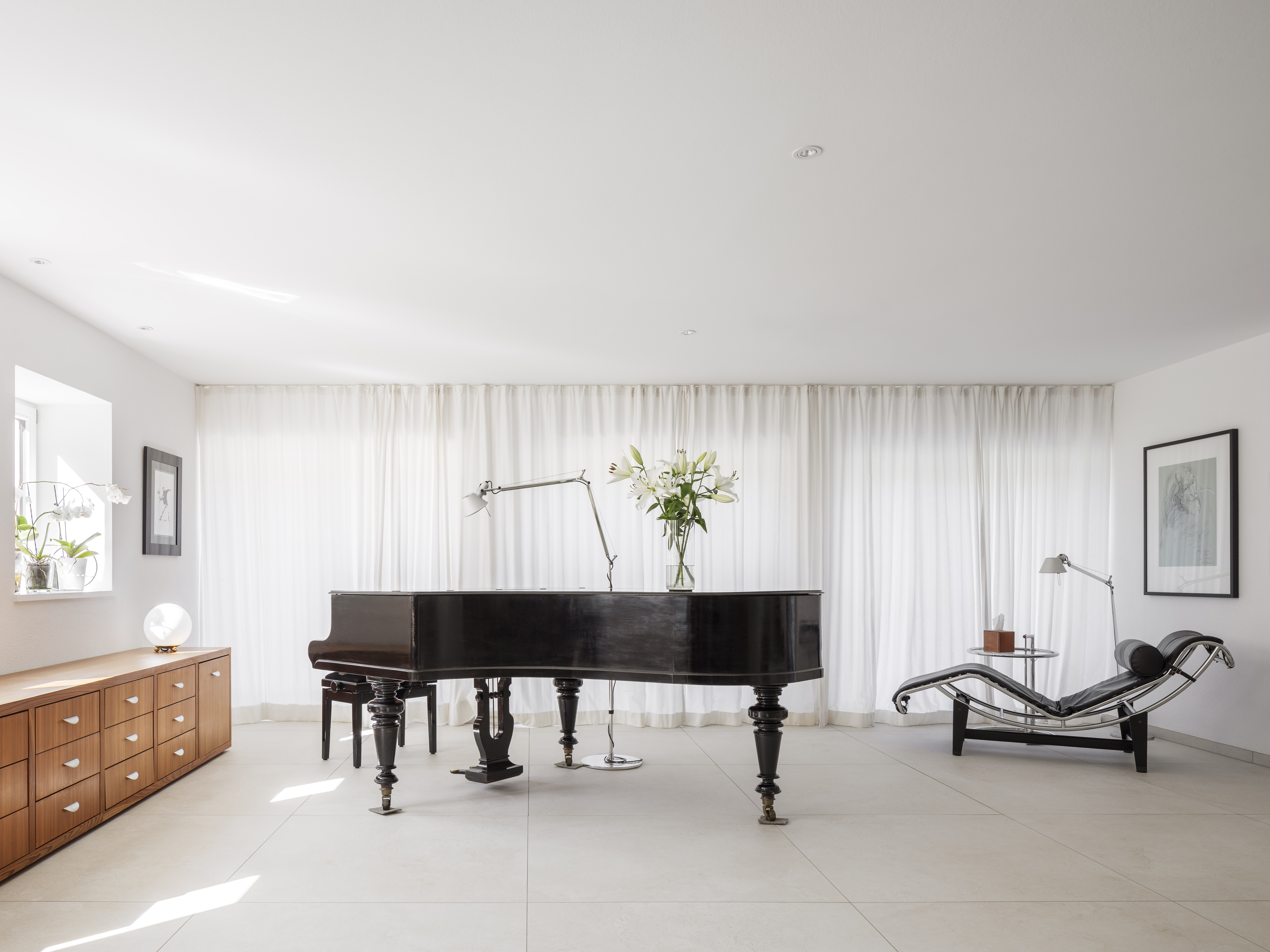 Bright, modern room with large-format floor tiles, grand piano, and designer furniture.
