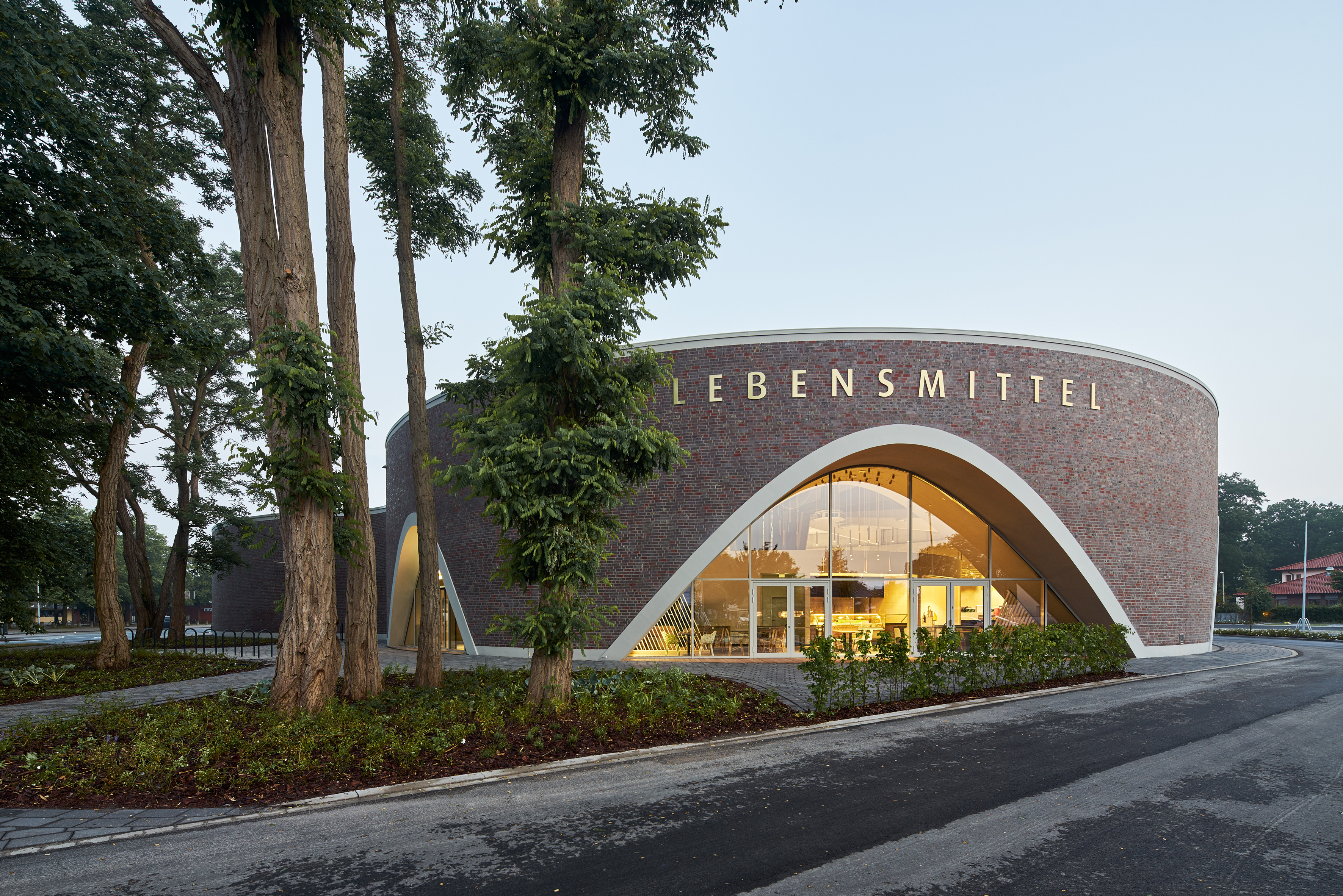 Modern building with curved brick facade and large glass front, surrounded by trees.