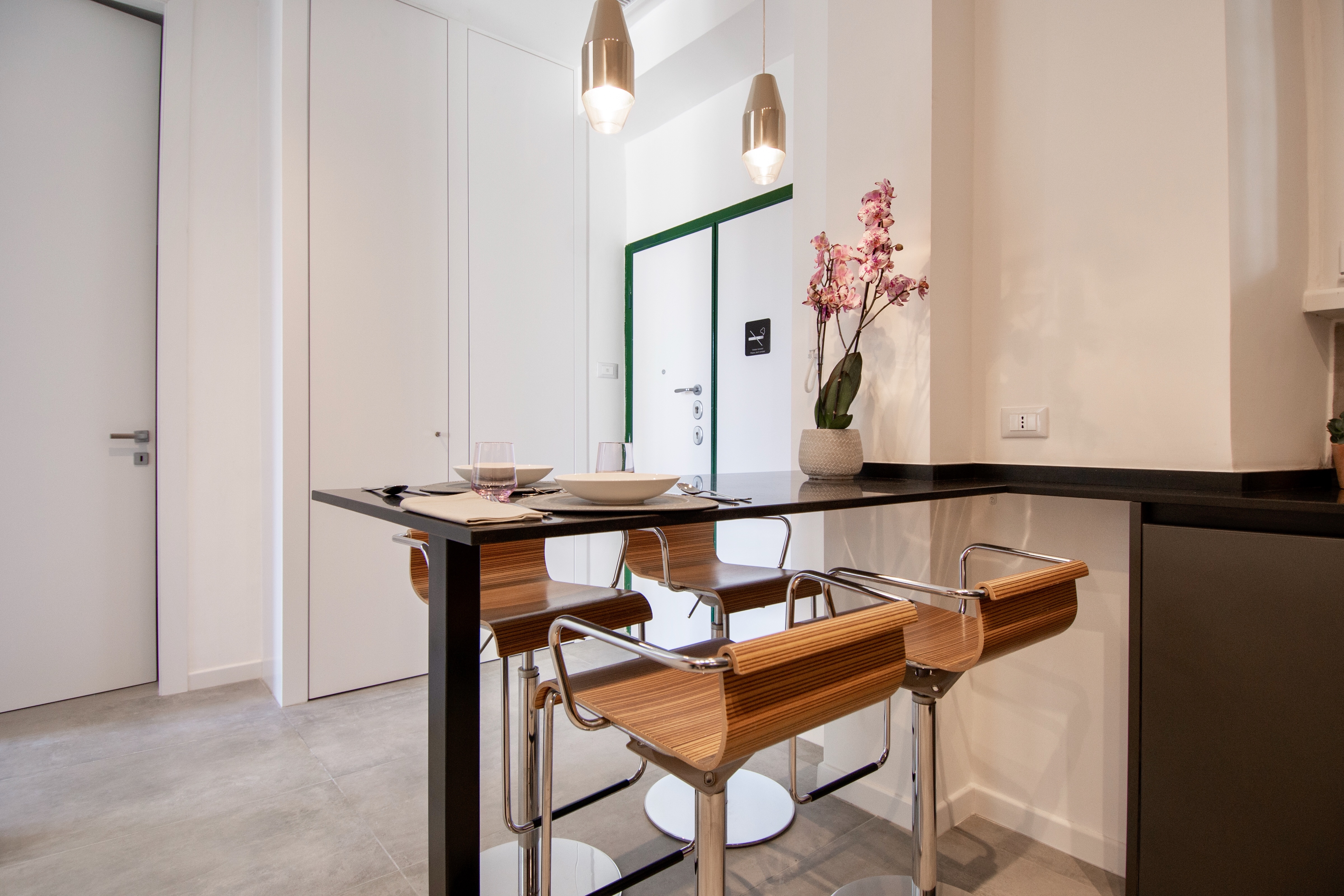Minimalist dining area with large-format grey tiles and wooden stools.